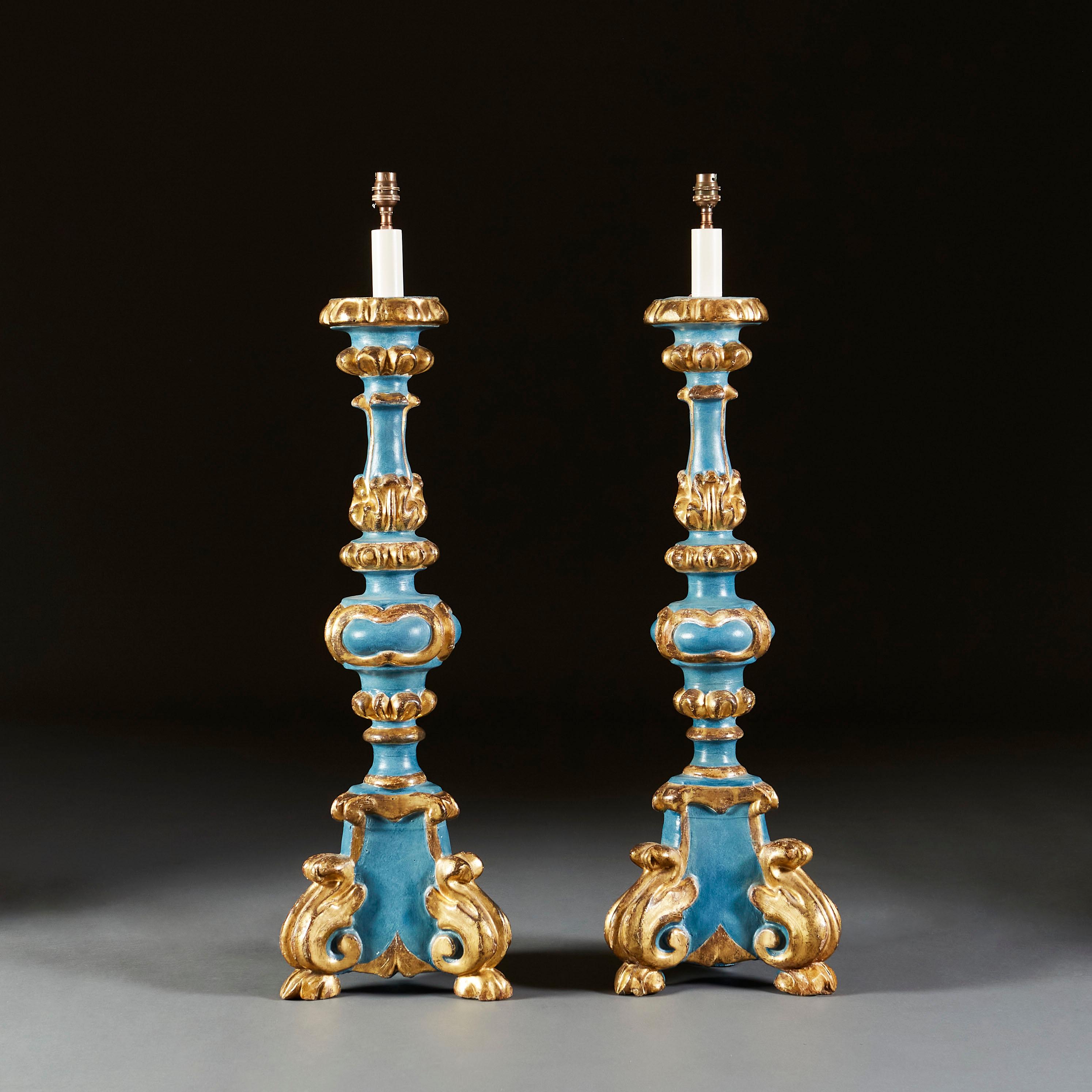 A pair of early twentieth century Italian candlesticks of large scale, with blue painted ground overlaid with carved and gilt decoration, supported on tripod bases with acanthus leaf scrolling feet.

Currently wired for the UK with twisted bronze