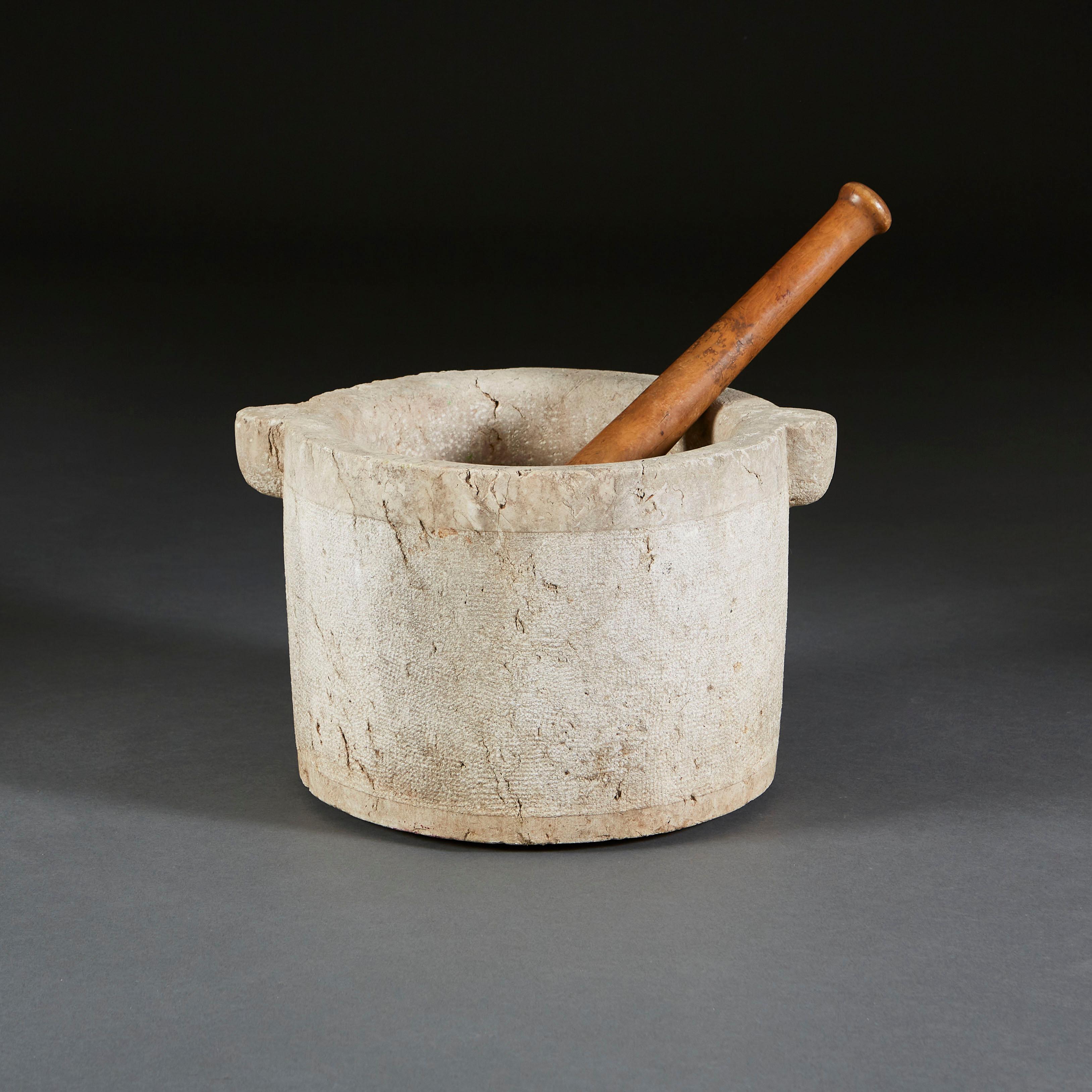 A mid-nineteenth century pestle and mortar of large scale, the mortar in stone with carrying handles to each side, accompanied by carved wooden pestle.