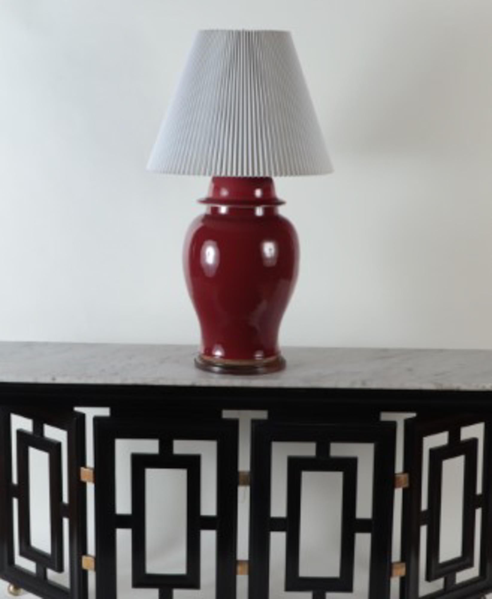 An oxblood vase with gilt wood base table lamp. Antiqued finish hardware includes double sockets with on/off pull chains, adjustable height rod, and cord with on/off switch.
