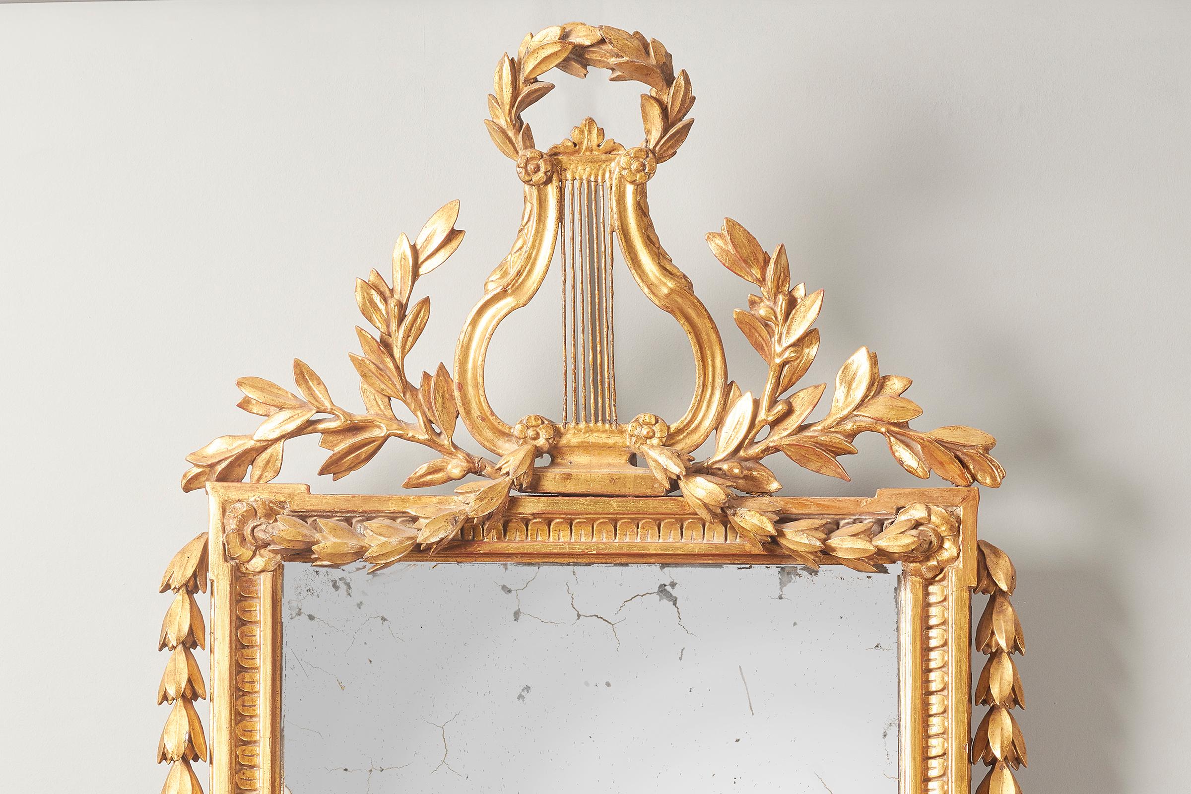 A pair of Spanish carved giltwood mirrors, late 18th century. Each with foliate hung lyre-cresting above a rectangular plate, with mask-centred lower frieze.