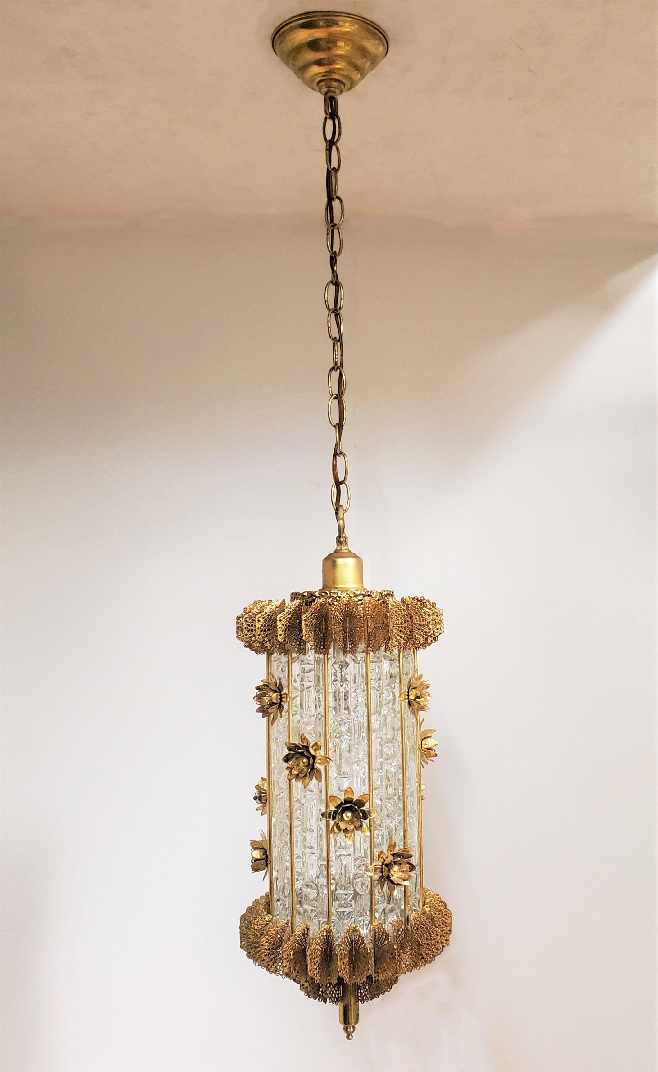 An unusual lantern style hanging fixture characterized by open work butterfly wings resulting in a pierced, netlike fringe which decorates the top and bottom circumference of this cylindrical chandelier like a crown. Blossoming flowers adorn the
