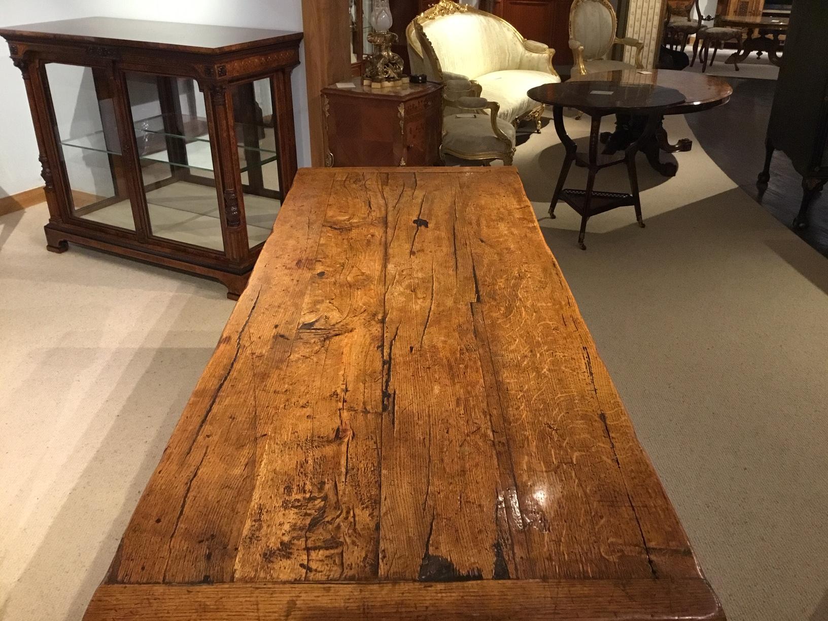 An unusual 19th century Primitive trestle end dining table. Having a three plank thick rustic oak top with cleated ends, raised on trestle ends united by a wonderful rough central stretcher with pegged ends. English circa 1880 in the 17th century