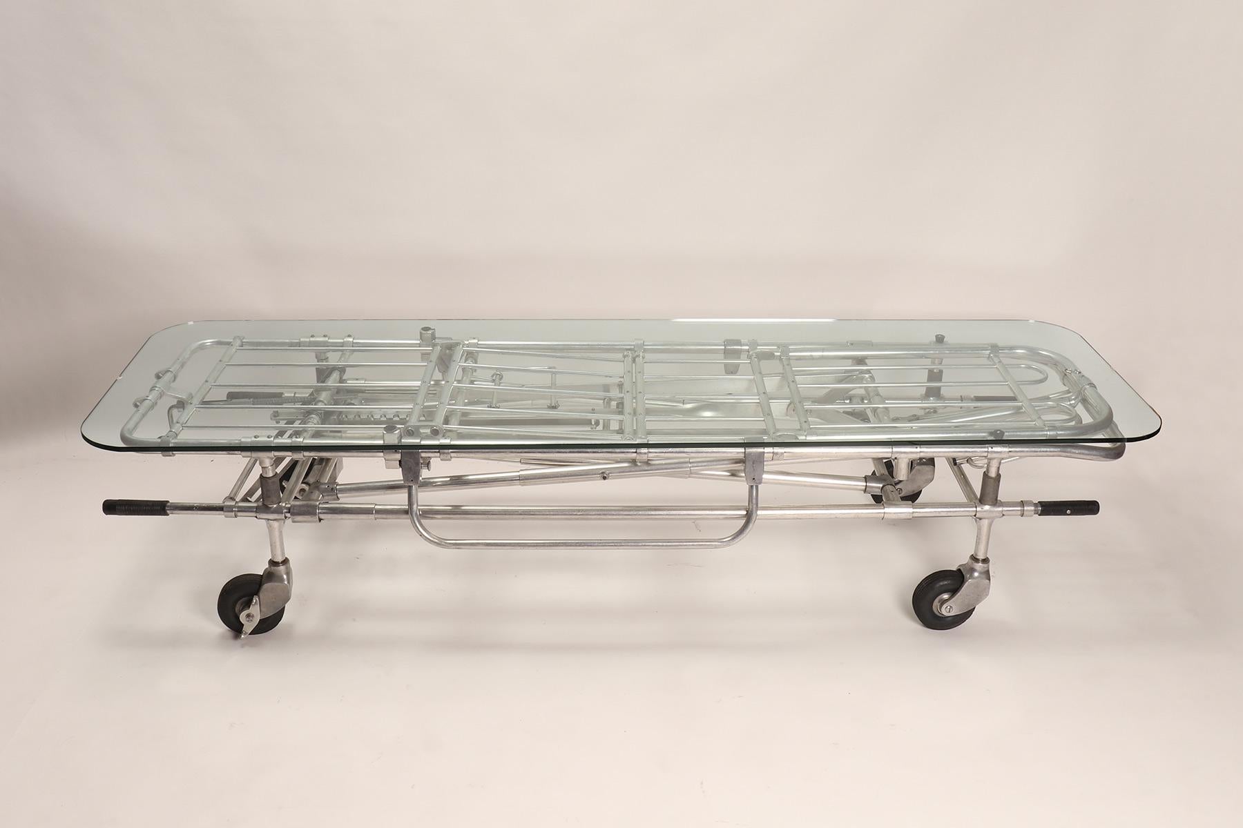 A fine example of reinterpretation and realization of an old element. A chrome metal gurney from an ambulance with wheels has been reused as a basis of an adjustable dining or coffee table, from 16 inches to 40 inches. The tabletop is made out of