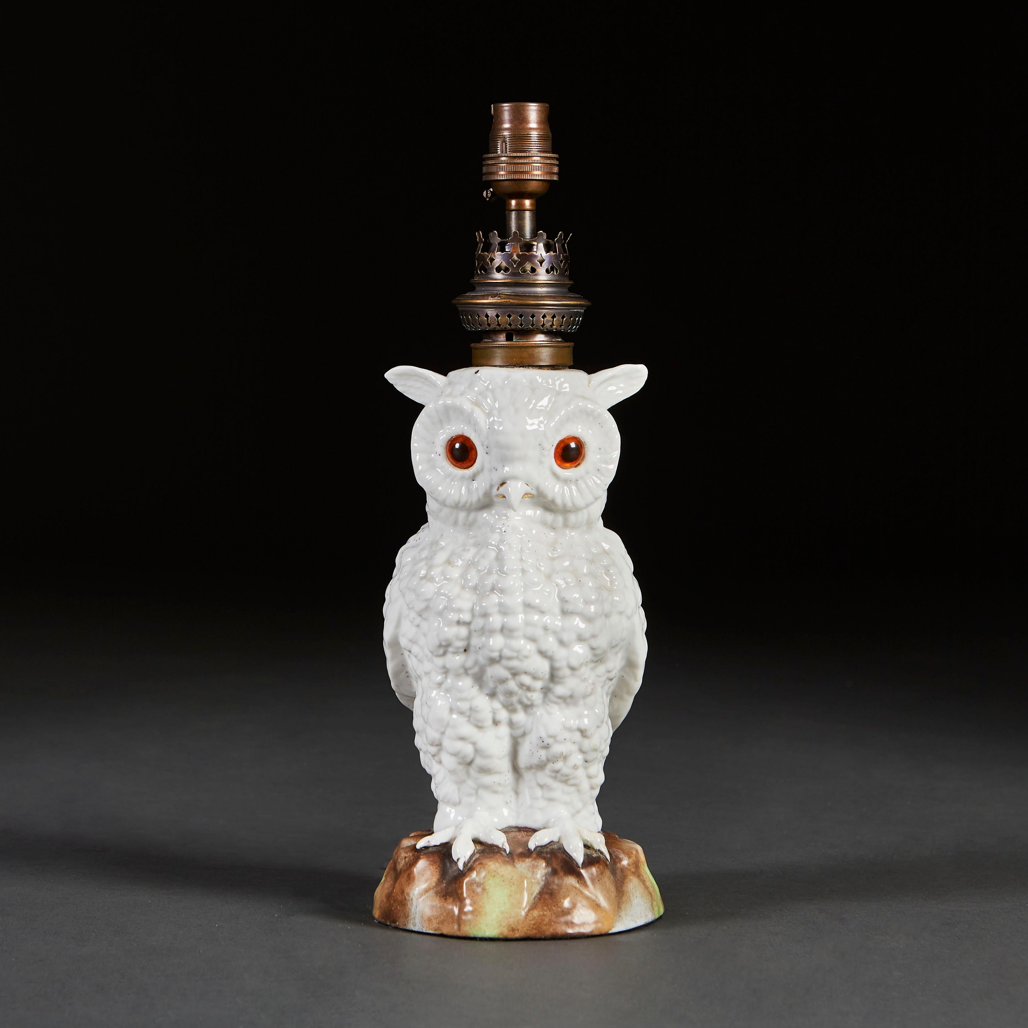 An unusual nineteenth century ceramic lamp in the form of an owl, modelled realistically perched on a rock, with wings folded behind, the owl with white glaze and glass bead eyes inset.