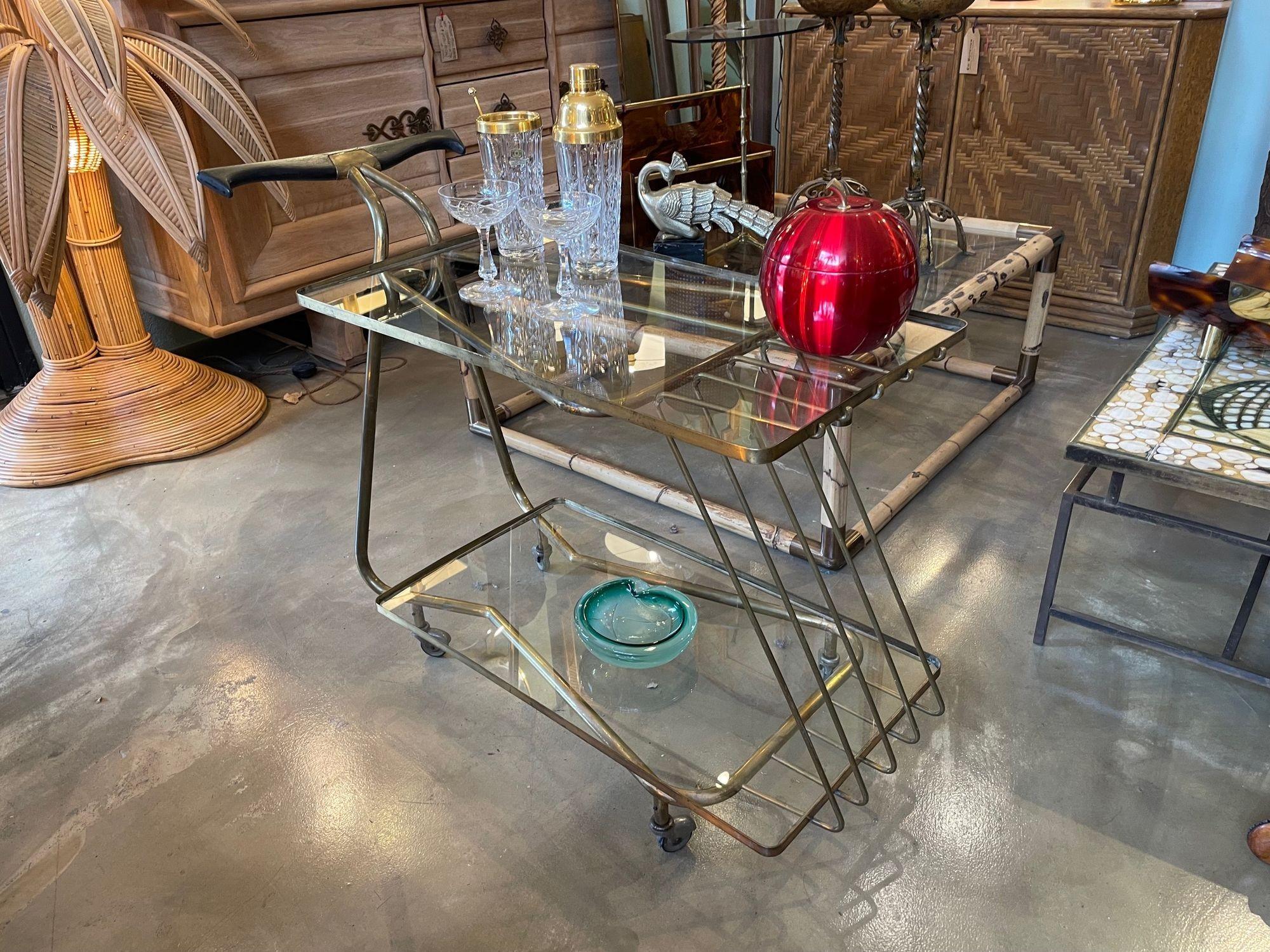 An unusual designed Italian 1950s brass bar trolley by Cesare Lacca with two glass shelves supported by solid brass frame with ebonised shaped wooden handle on orignal brass castors.
