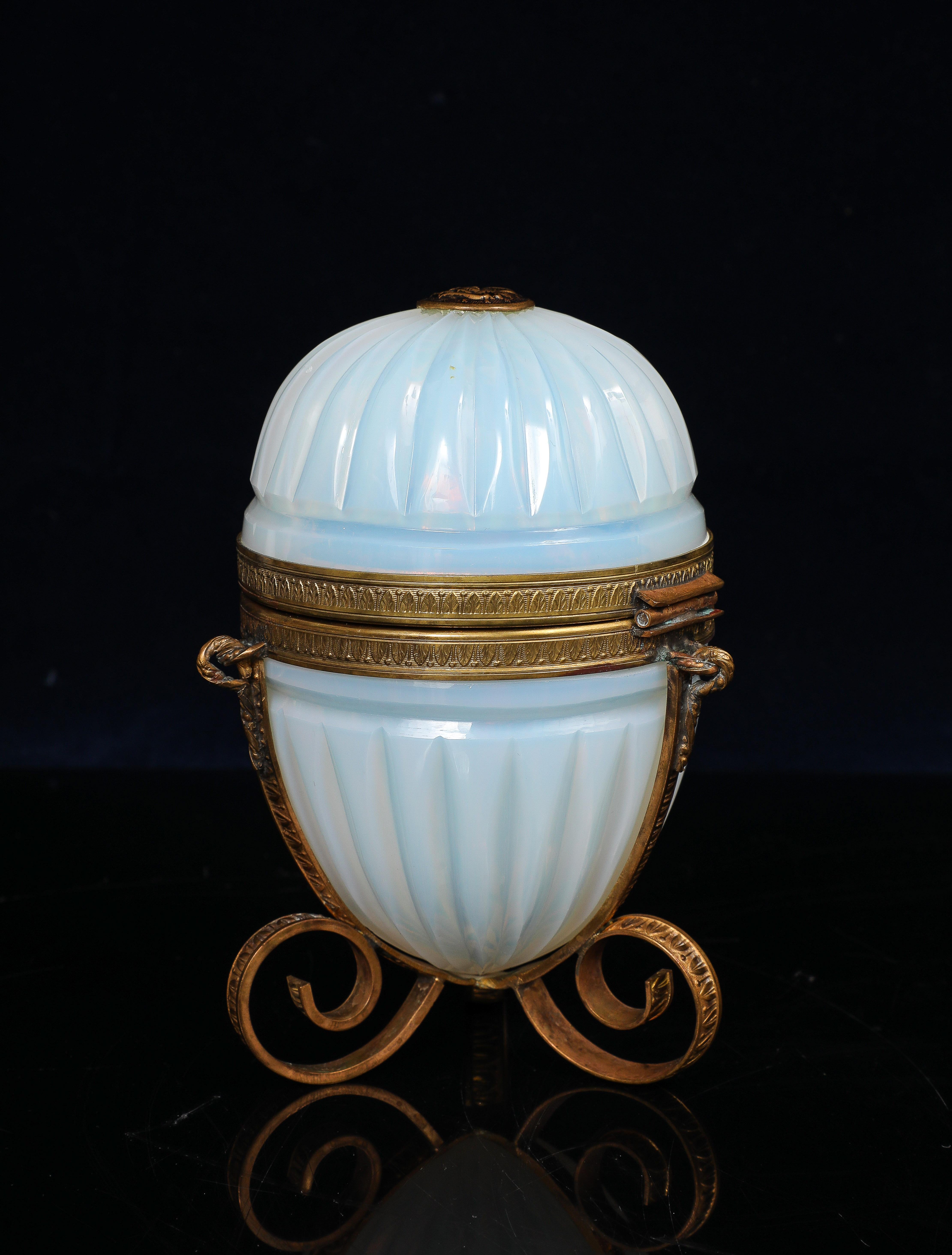 A highly unusual and exquisitely crafted French egg-form covered box, attributed to Baccarat and dating to the mid-to-late 19th century, composed of luminous white opaline crystal and mounted in intricately cast and fire-gilded bronze. The ovoid