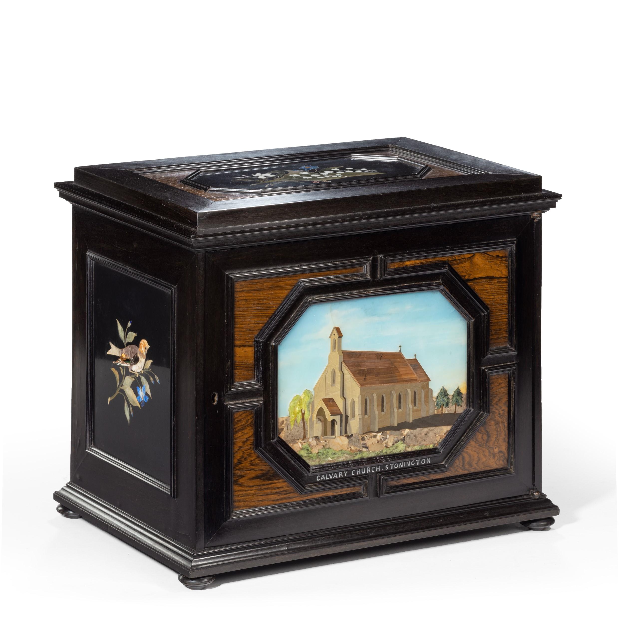 An unusual ebony bijouterie table cabinet showing Calvary Church, Stonington, Long Island, of rectangular form with two cupboard doors enclosing a dummy drawer, which disguises a hidden compartment under the top pietra dura panel, three long