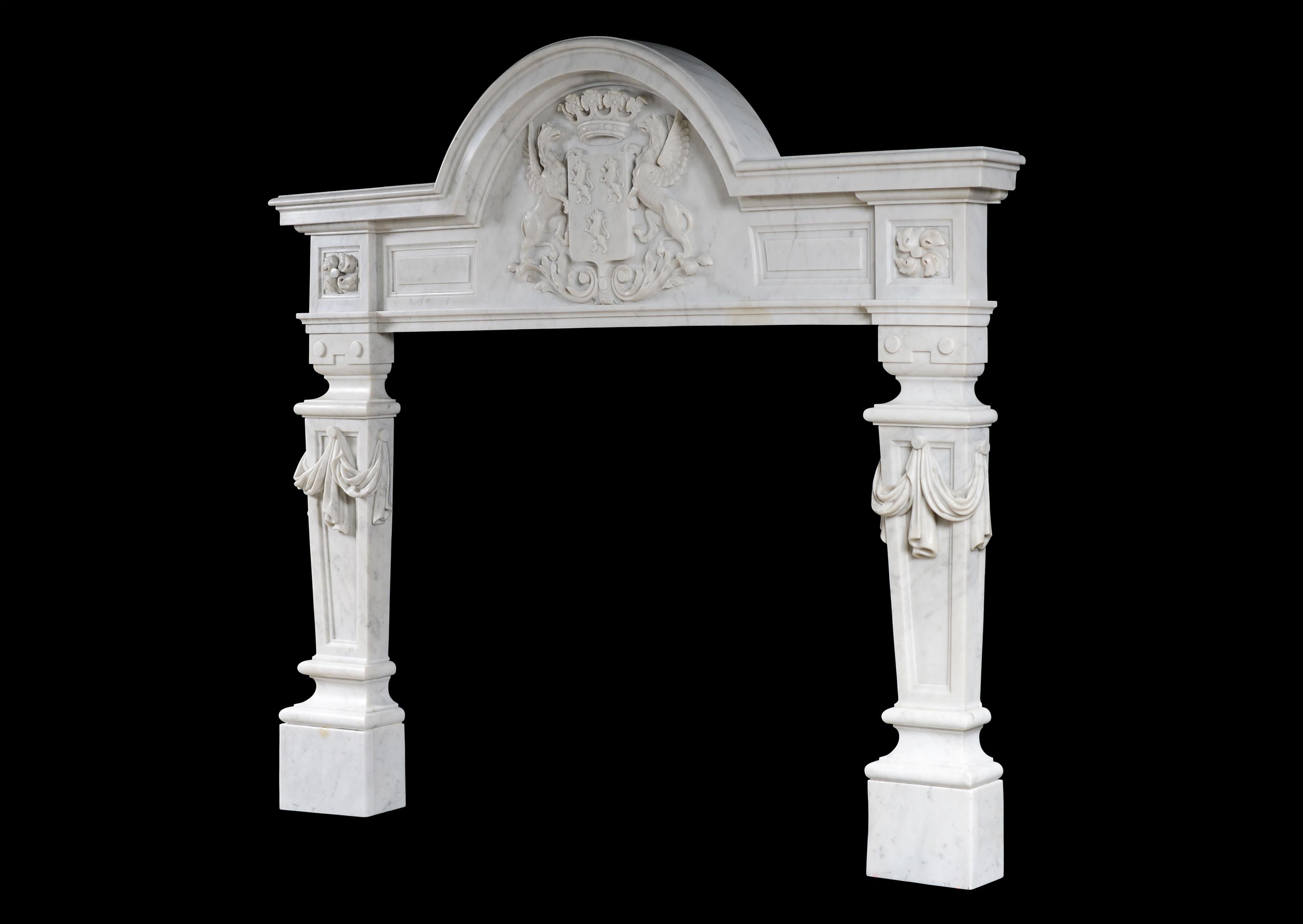 An unusual English Baroque style fireplace in Italian Carrara marble. The substantial frieze with a coat of arms featuring griffins and shield, with swirling floral paterae to end blocks. The tapering, panelled jambs with fine quality carved