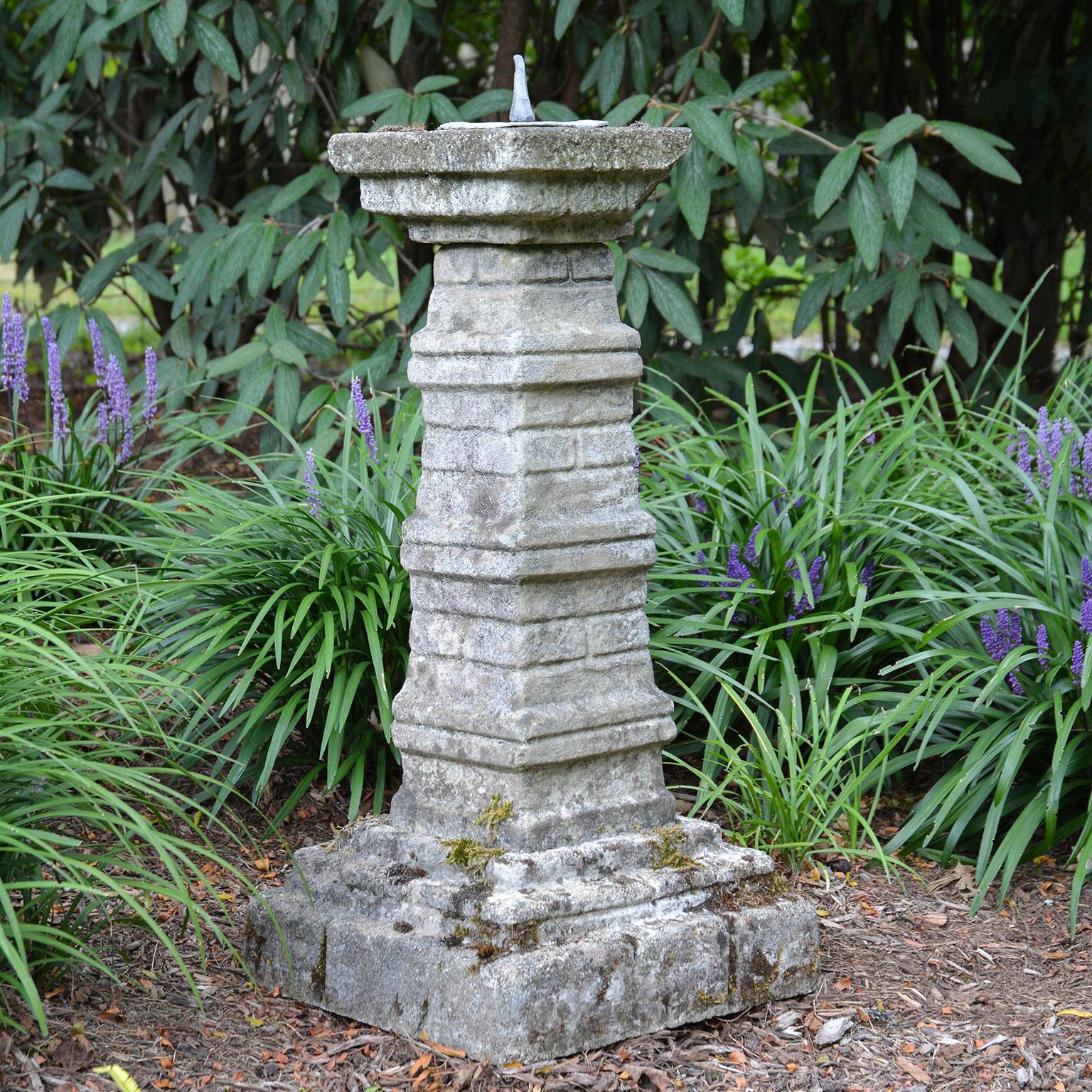 A composition stone sundial pedestal, the body having the appearance of stacked slabs of varying dimension, with lead dial plate.