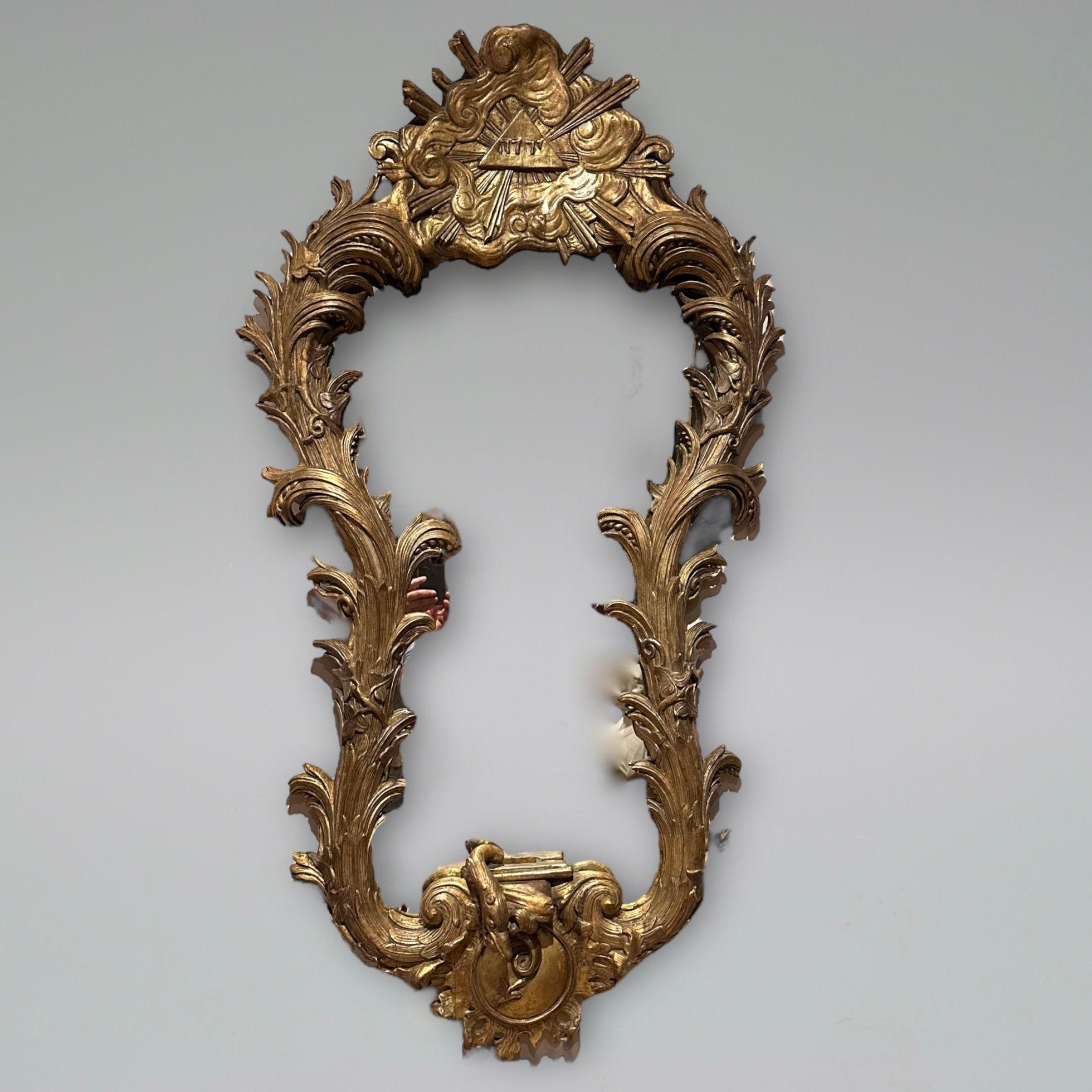 Miroir de bonne taille en bois doré sculpté du XVIIIe siècle, avec un motif hébraïque entouré de nuages et d'un rayon de soleil, la plaque façonnée avec des feuilles d'acanthe profondément sculptées et un serpent en dessous. 
Circa 1770
