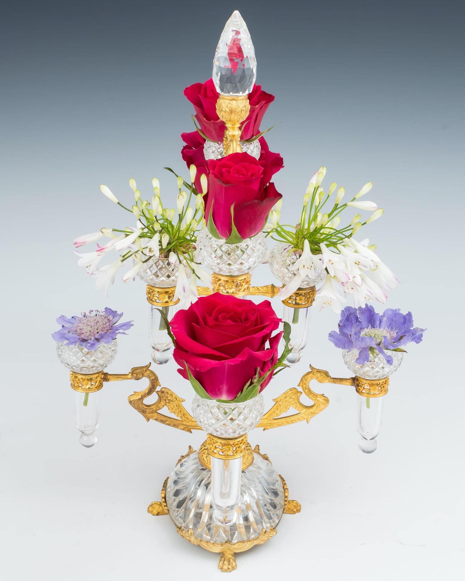 The ormolu mounted glass base on paw feet with central stem decorated with climbing ivy leaves issuing eight crane birds supporting diamond cut posy vases the epergne terminating with lapidary cut finial.
Measures: height 40.5 cm (16