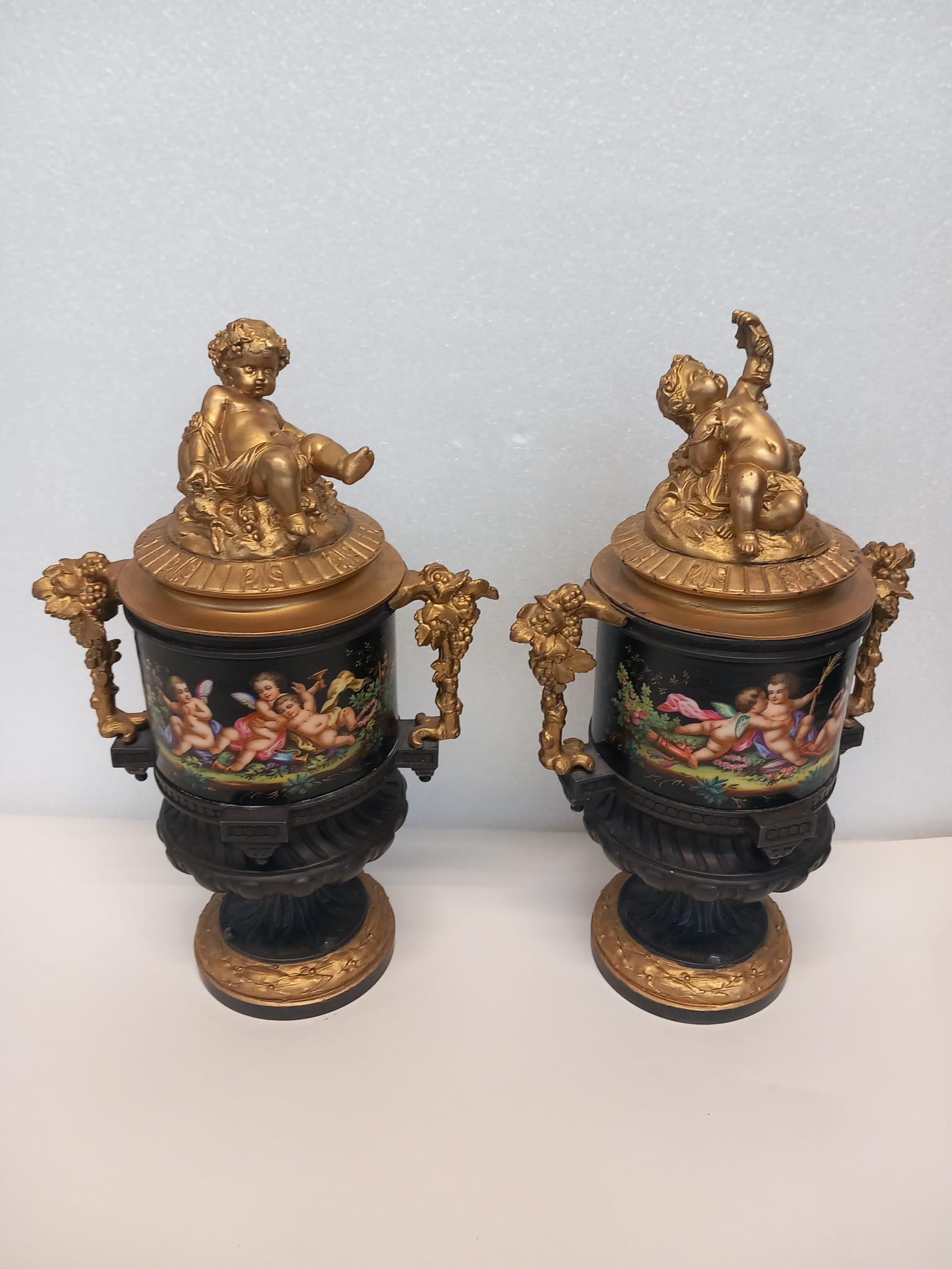 An unusual pair of  French vases hand painted in bright enamel colours of scenes of putti drinking and having fun . Decorated on a dark background with allegorical emblems on the back alluding to love. The bodies are adorned with good quality gilt