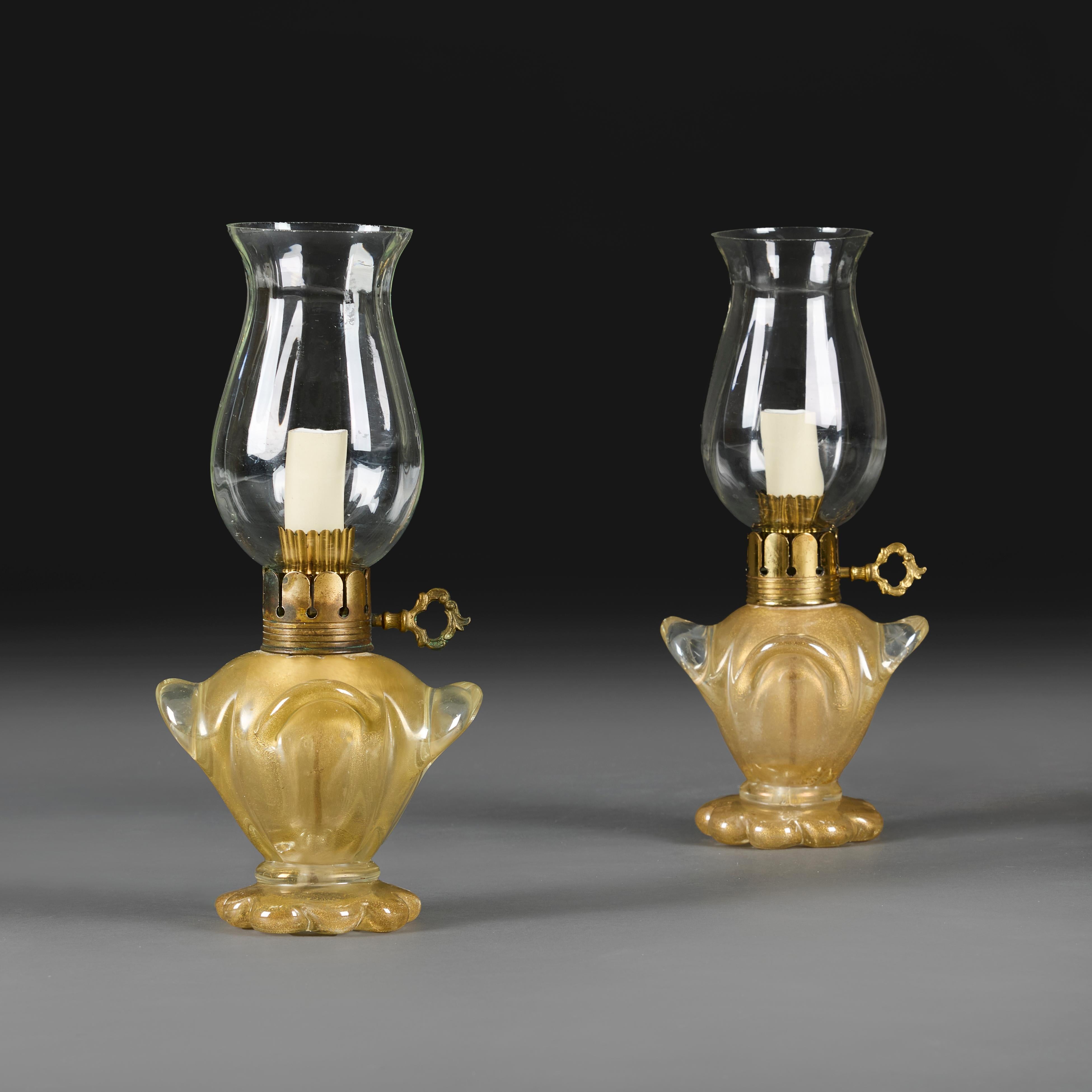 Italie, vers 1940
Une paire inhabituelle de lampes en verre doré de Murano, avec des bases festonnées et des poignées stylisées sur les quatre côtés, avec des montures en laiton d'origine et des abat-jours en verre en forme d'ouragan.

Hauteur