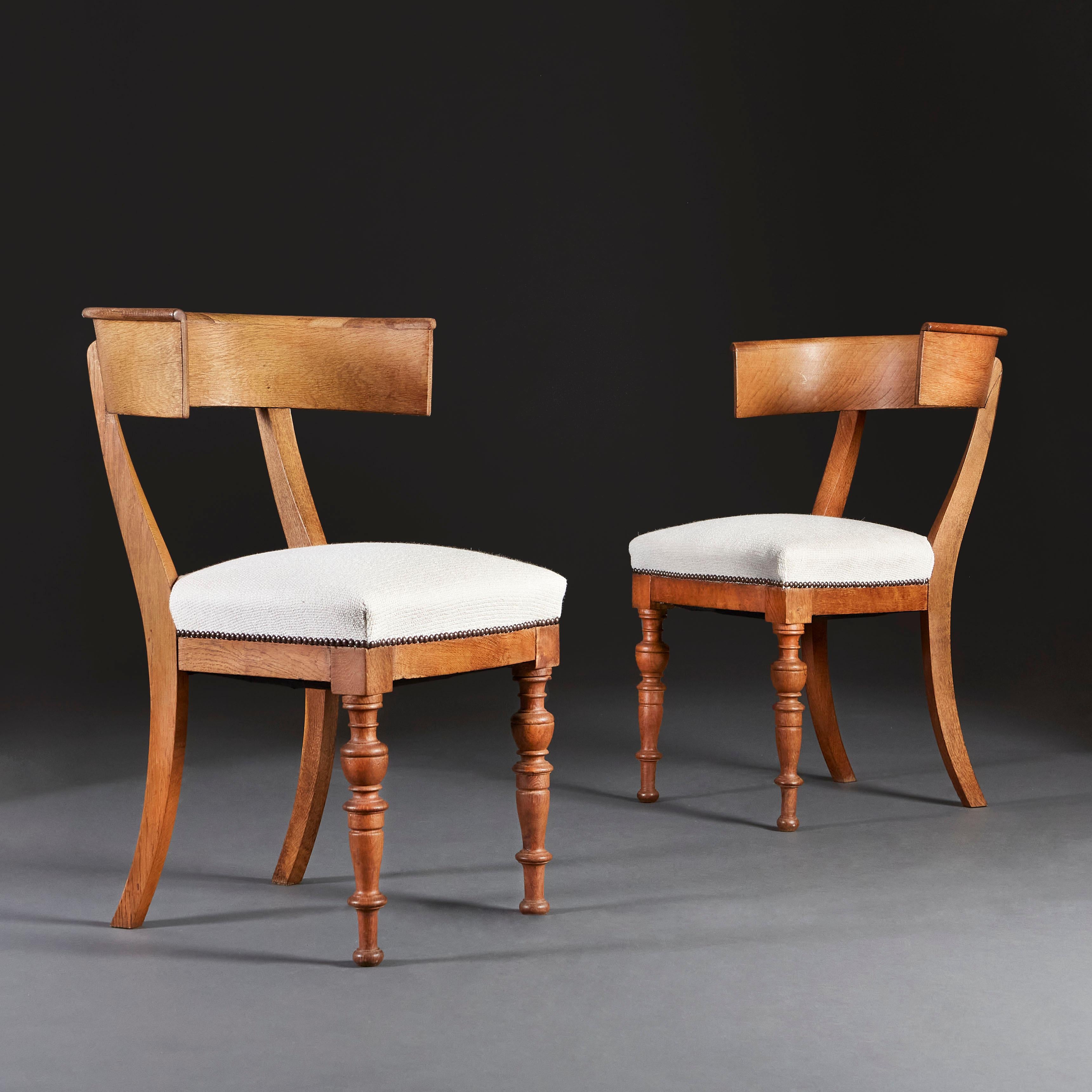 A pair of early 19th century oak Klismos chairs with curved backs, turned front legs and splayed back legs.