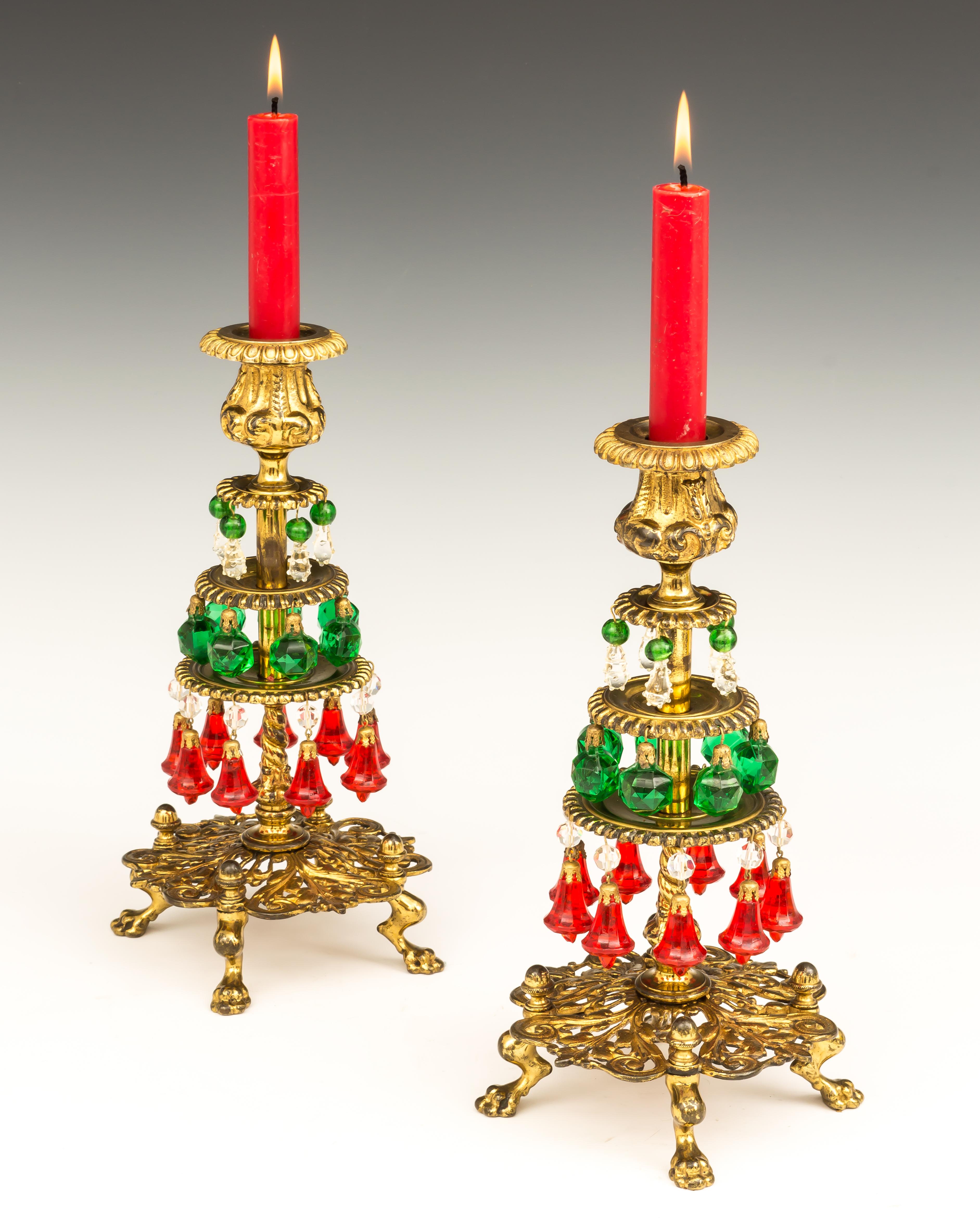 An unusual pair of Victorian Christmas candlesticks, the finely fretted base on four paw feet supporting three tiered dishes hung with colorful festive pendants.