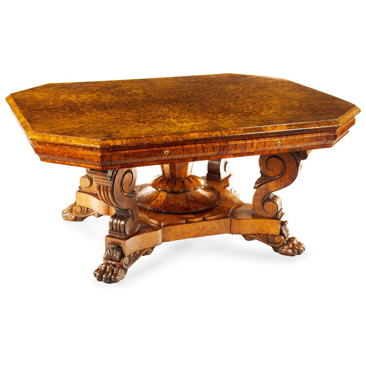 An unusual William IV amboyna and oak four drawer library table by Simpson, the rectangular top with cut corners and a shaped frieze disguising two cushion drawers on each side, raised on four powerful scroll legs and an additional tapered faceted