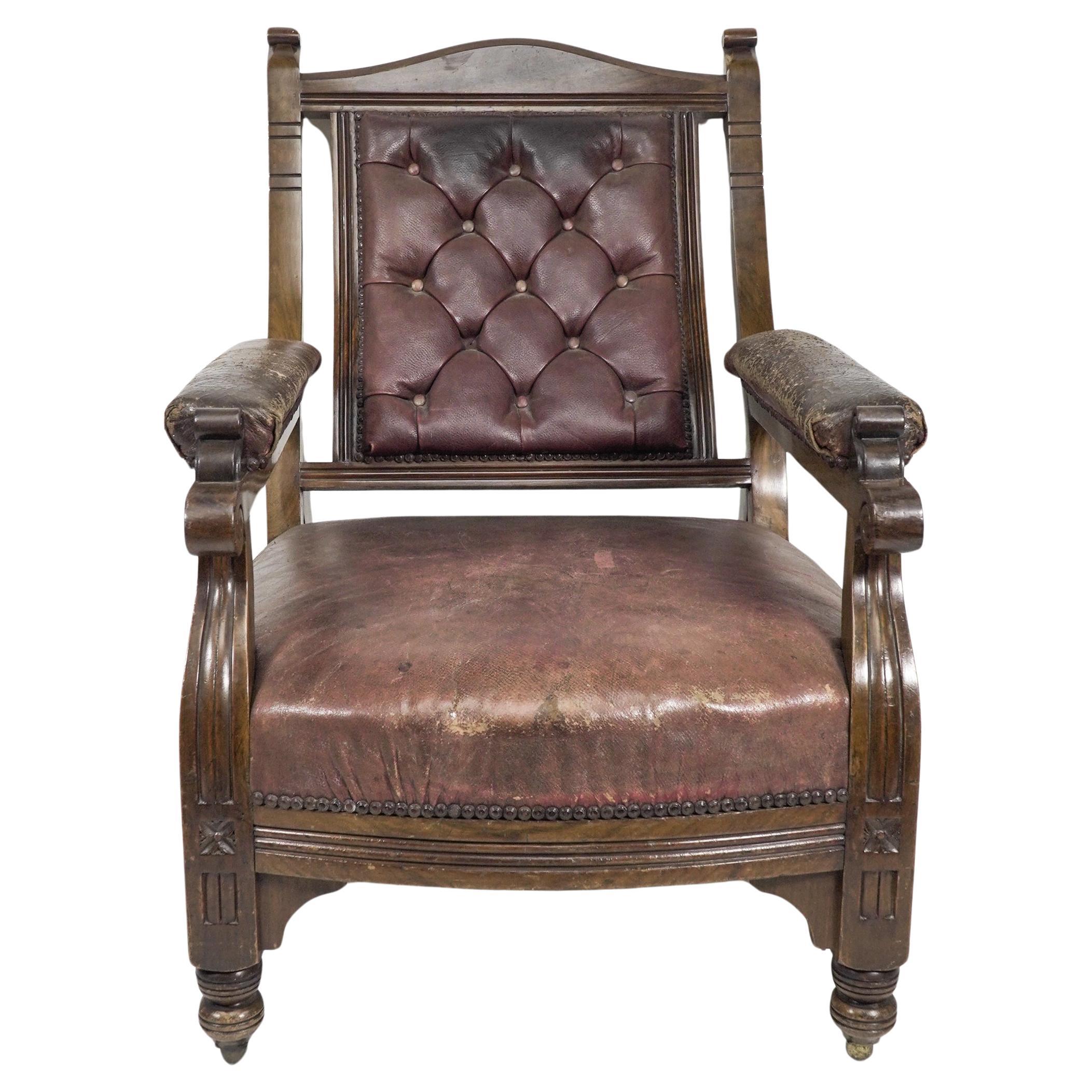 An Aesthetic Movement Walnut Library armchair with a curvaceous back and nicely worn button back leather upholstery. The arms with double curves to the end of the armrests and florets carved to the front legs and a strong architectural angular