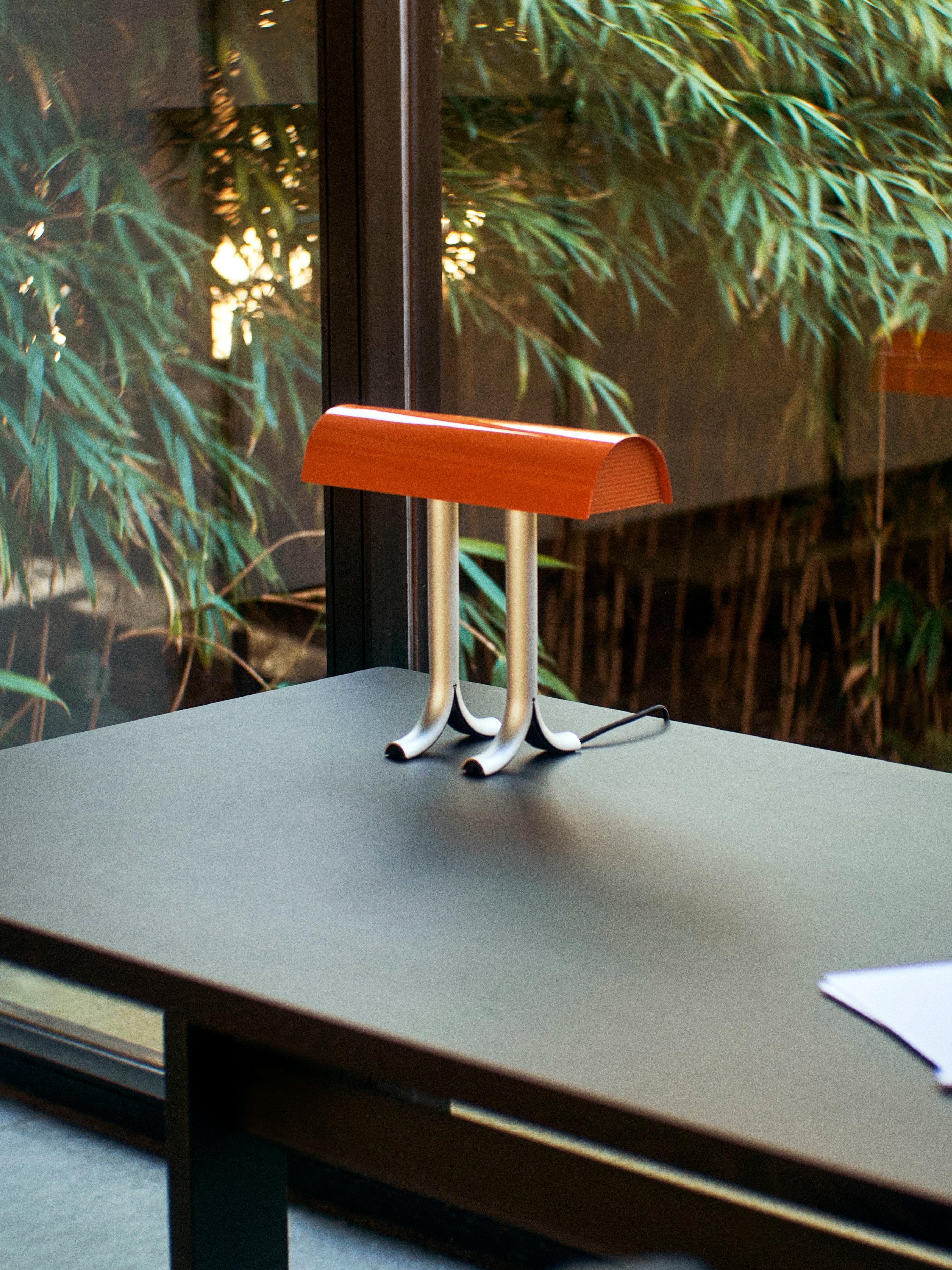 La lámpara de mesa Anagrama de Sam Weller fusiona funcionalidad y atractivo visual para crear una lámpara de mesa de construcción robusta y fuerte personalidad. 
Con una pantalla brillante generosamente curvada que se asienta sobre dos patas de