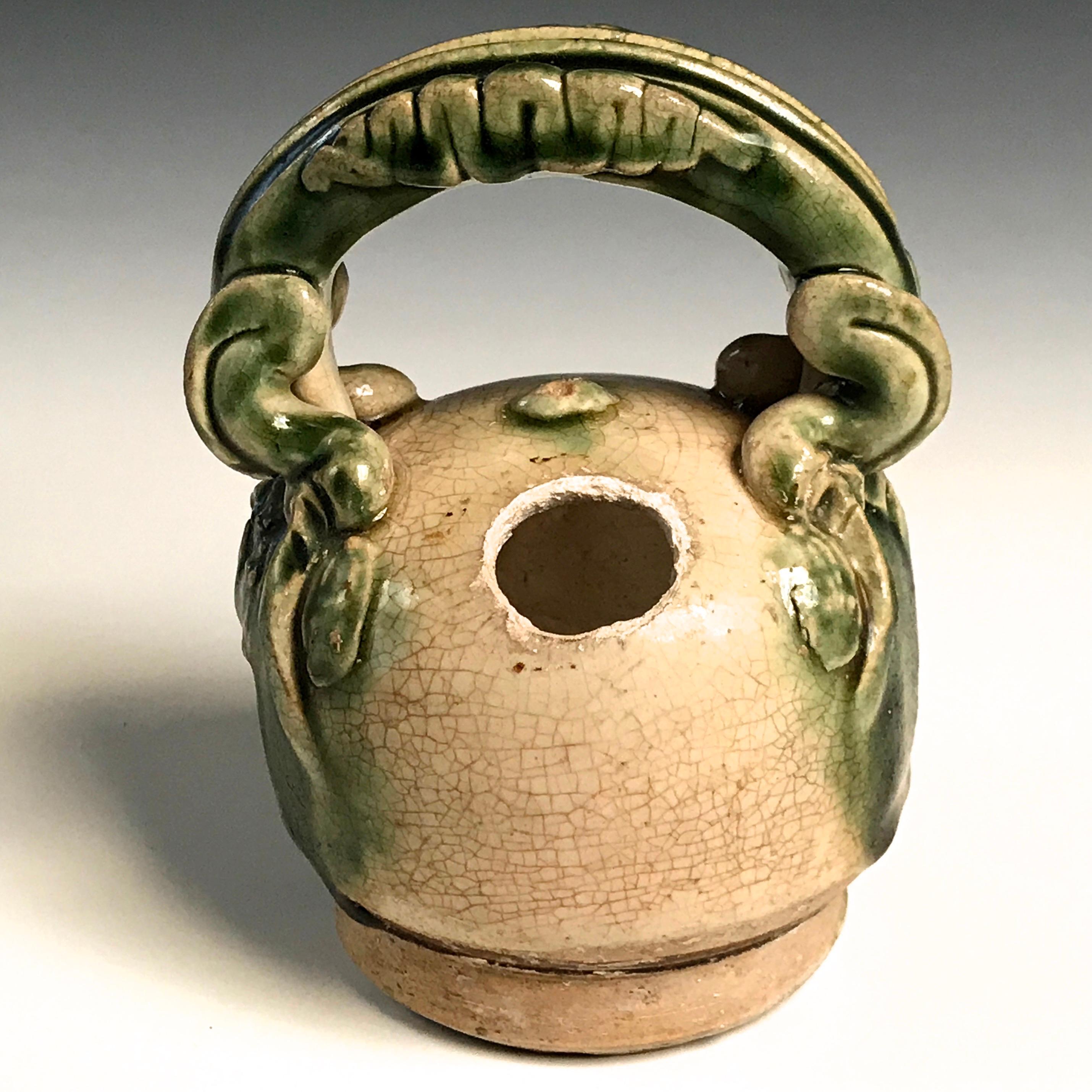 Anamese three-color ware ceramic lime pot for slaked lime a component for the social practice of chewing “Betelnut”, globular form resembling an areca nut with round aperture at the shoulder and decorative overhead handle stylized in such a way that