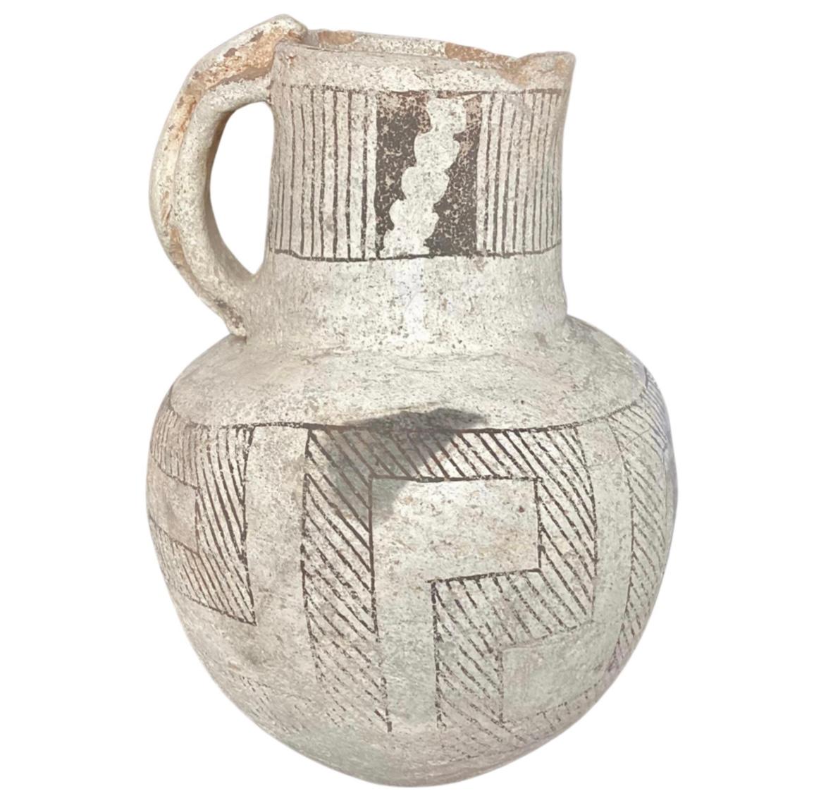 Stunning piece of Native American pottery. Pitcher has a round body and a thick handle that includes an applied snake. The white-ground exterior features a band of vertical lines and serrations presented in an applied black pigment. Believed to be
