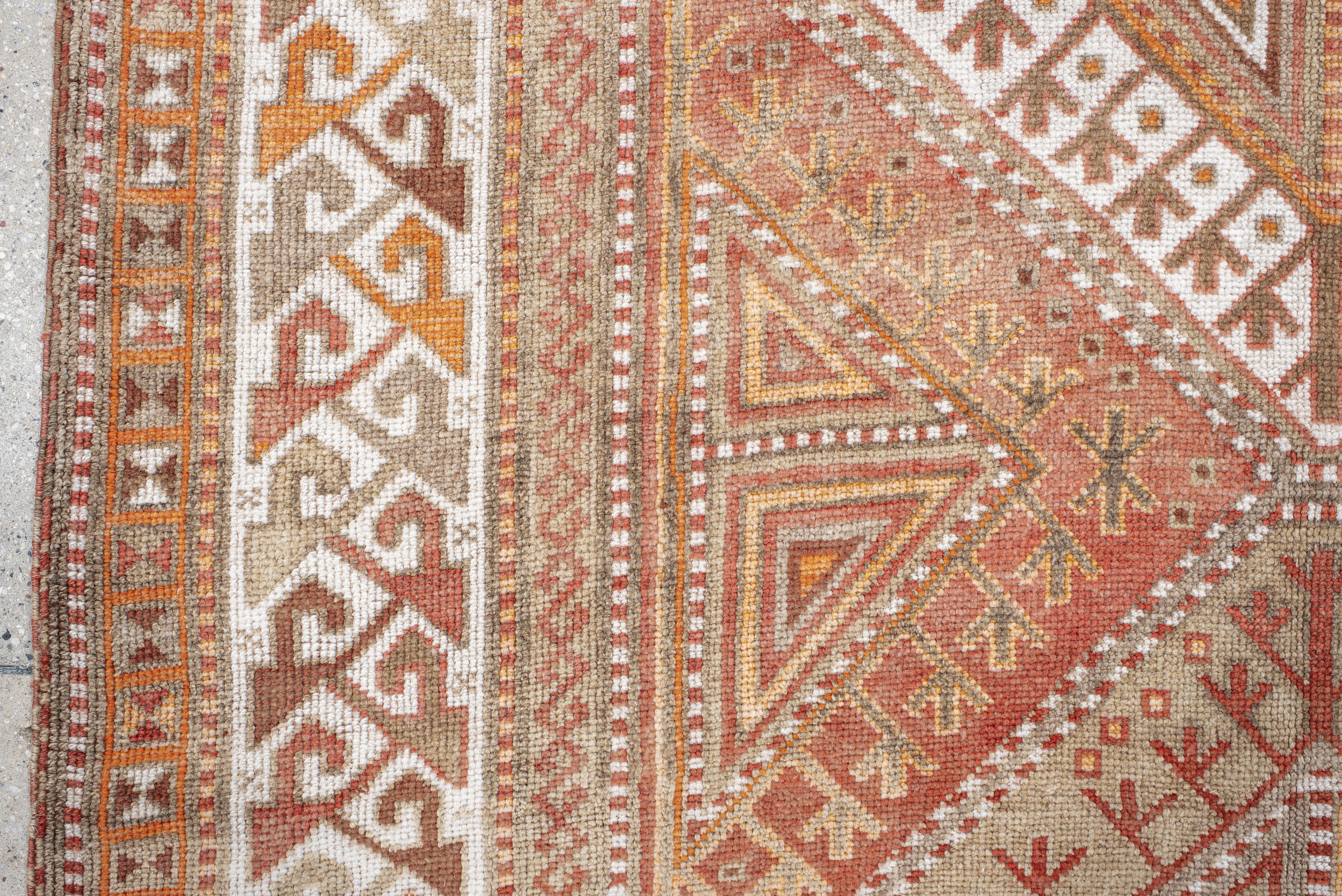 Dieser handgeknüpfte Vintage-Teppich aus Anatolien, der mit traditioneller Kunstfertigkeit hergestellt wird, zeigt eine dynamische Abfolge geometrischer Rautenmedaillons, die in einer warmen Farbpalette gehalten sind. Der Sockel ist in erdigen