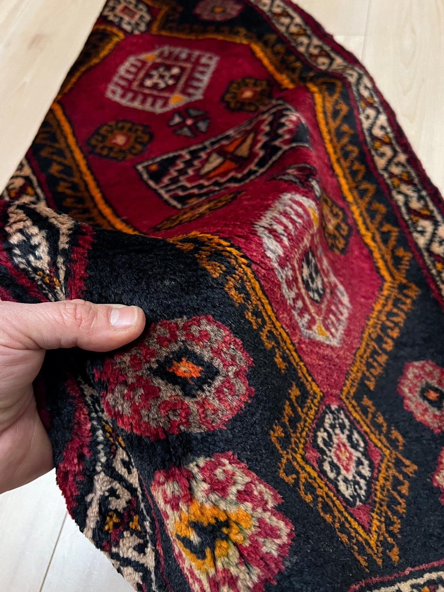 Una minialfombra turca vintage llena de carácter, tejida a mano con suave lana hilada a mano y con un atrevido emblema tribal central enmarcado por tonos rojo rubí, carbón, ocre cálido y nogal terroso. Su tamaño compacto lo hace perfecto para