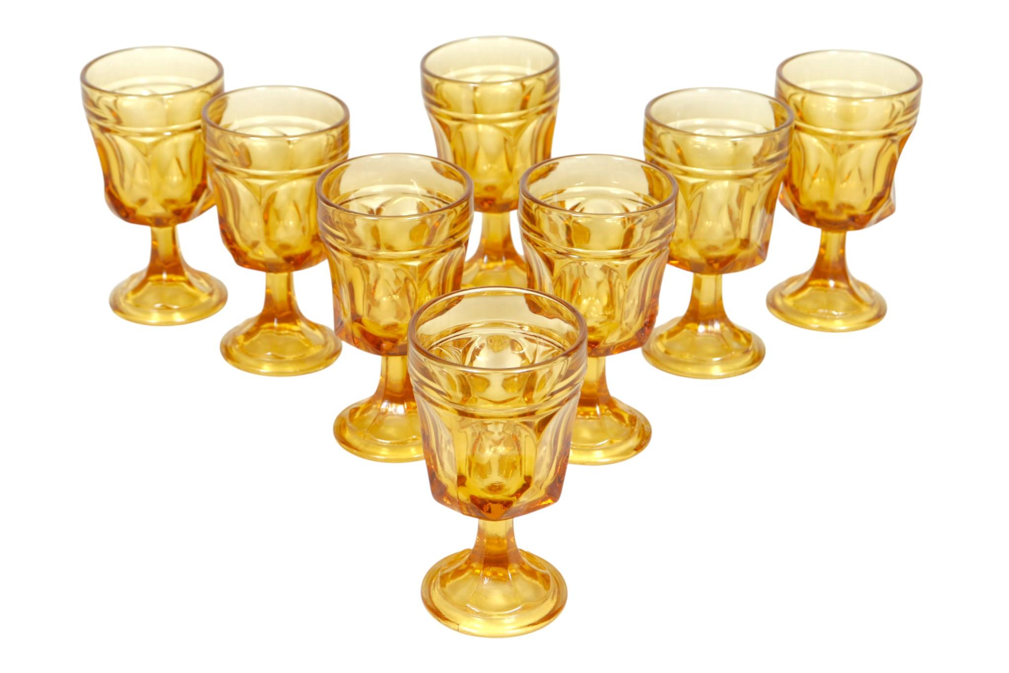 A set of eight Anchor Hocking Fairfield amber glasses. Sculptural cut glasses are decorated with concave sides and a scalloped stem and foot. Dimensions per glass.
