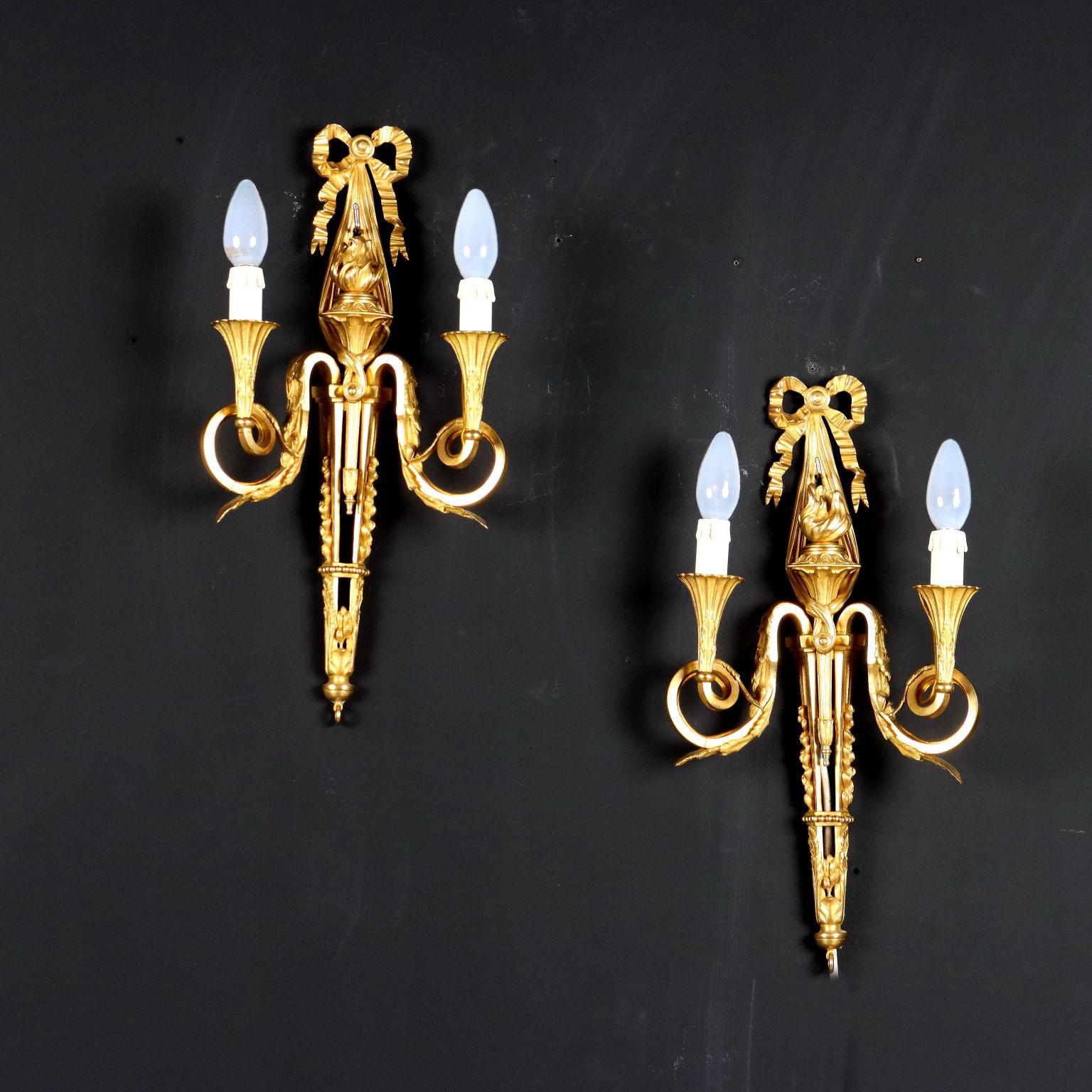 Pair of two-light wall sconces with gilded bronze frame. Central torch supported by a festoon culminating in a love knot and stopped by galls. Italy 20th century.