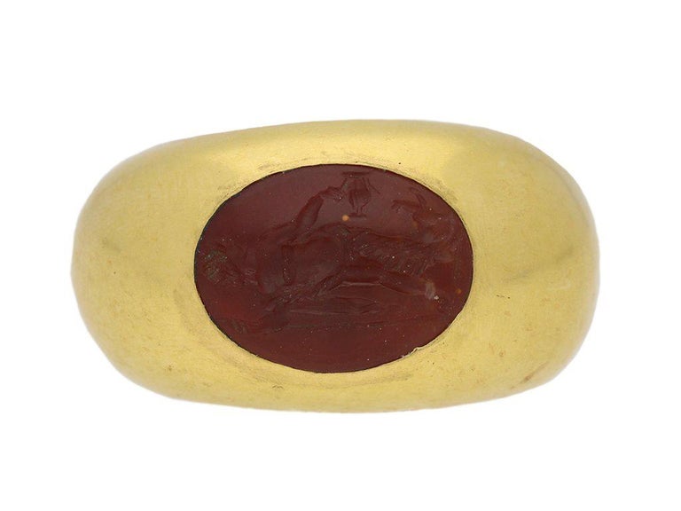 Ancient Roman Dionysus intaglio ring. Set with an oval carnelian intaglio finely engraved with standing figure of Dionysus holding a thrysus and drinking cup, in a closed back rubover setting, with smoothly rounded trumpeting shoulders tapering