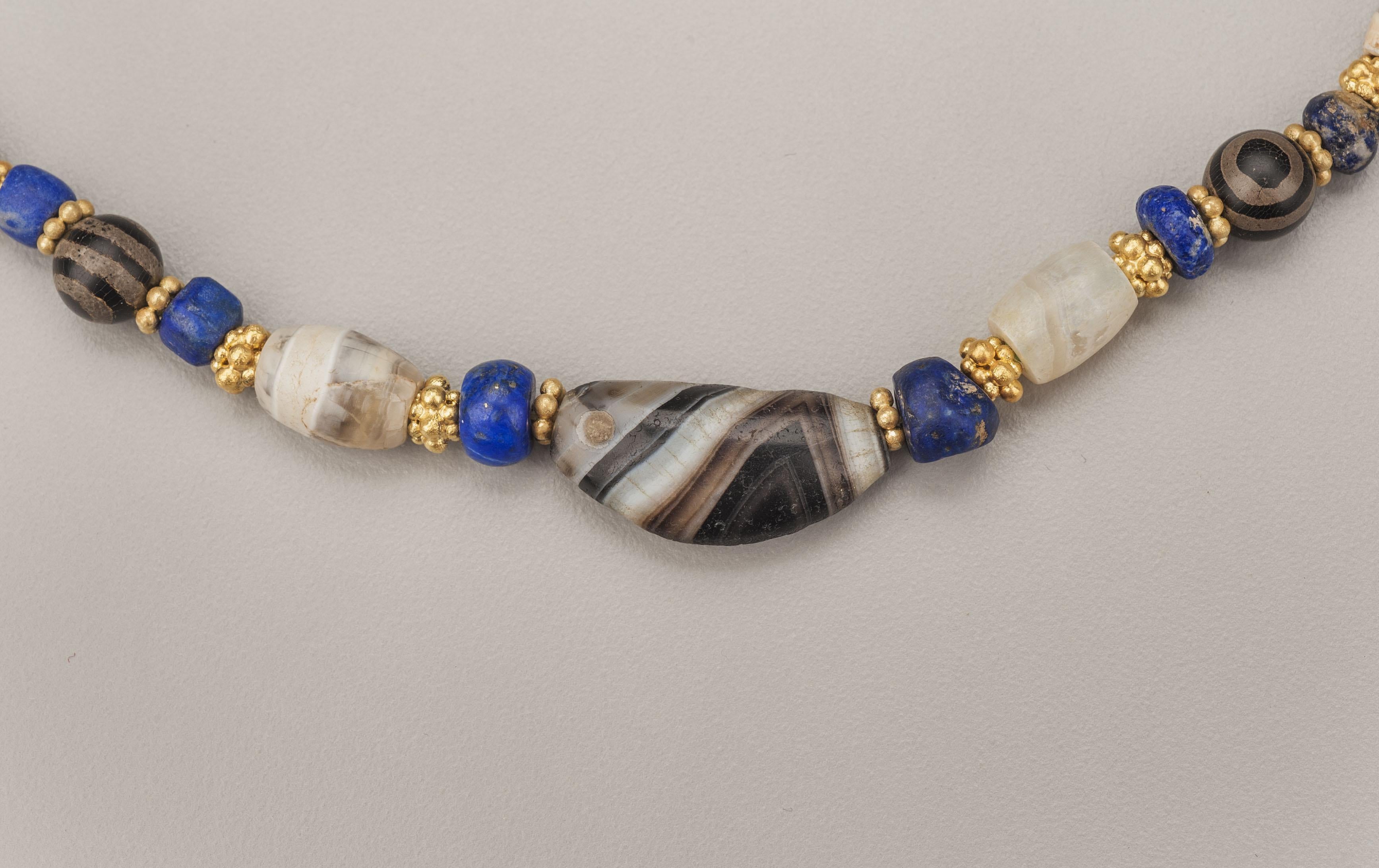 Sixteen agate barrel beads each faced with a three layer gold granulated bead alternating with fourteen spherical etched agate beads each faced with a pair gold granulated ring beads and a pair of small lapis lazuli beads. The center agate bead in