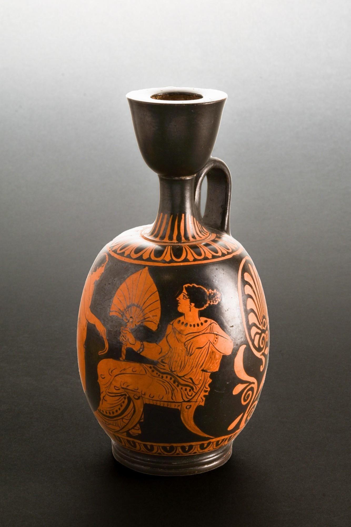 This rare ancient Apulian Iliupersis pottery vase unveils a traditional scene; a young woman seated, dressed with a delicately draped garment, gracefully holding a fan. In front of her stands a caped man holding a strigil. The piece is accompanied