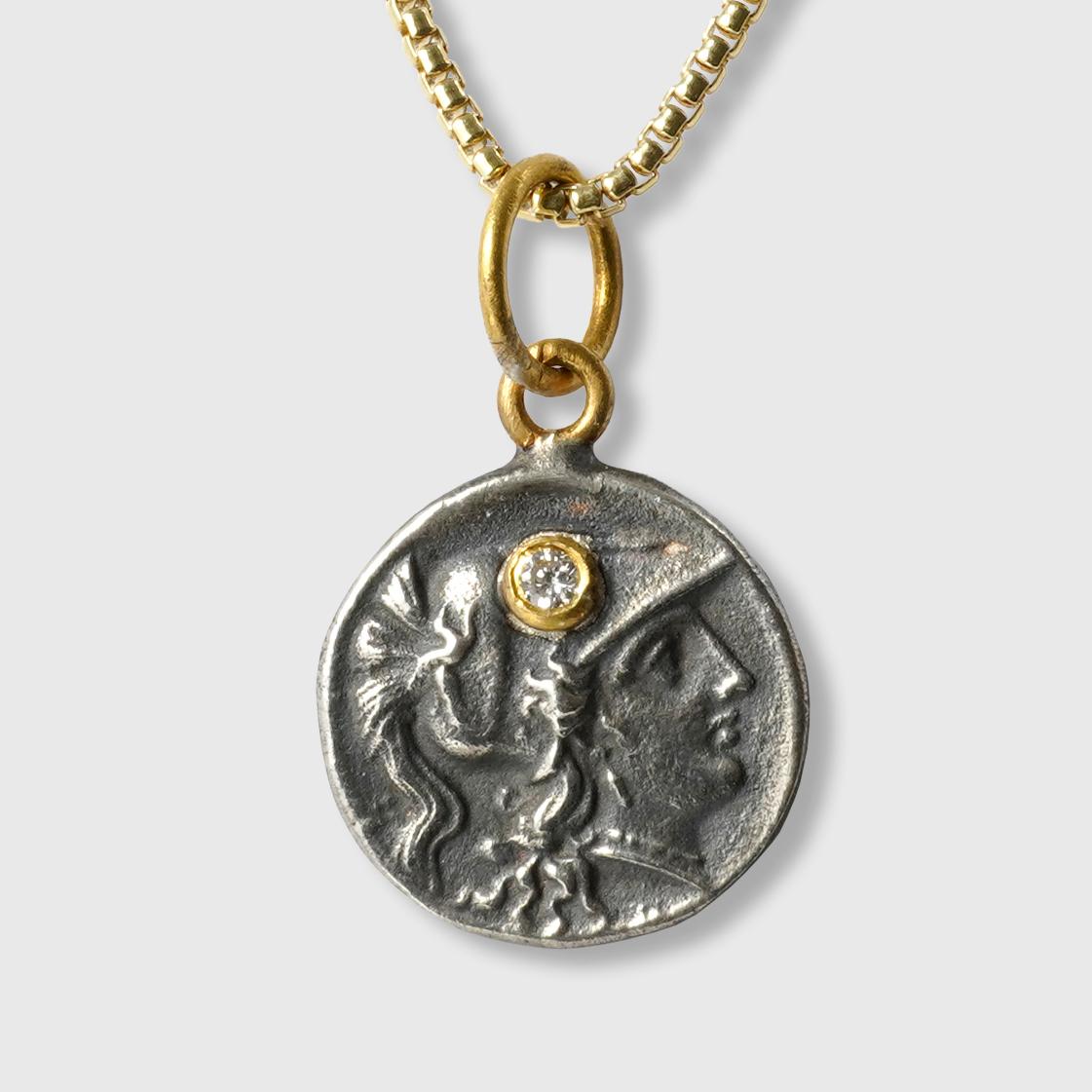 Pendentif en or 24kt, argent et diamant de 0,01ct en forme de tétradrachme (réplique de la pièce d'Athéna).

L'HISTOIRE : 
Athéna était l'une des douze principales divinités de l'Olympe et la déesse associée à la sagesse, à l'artisanat et à la