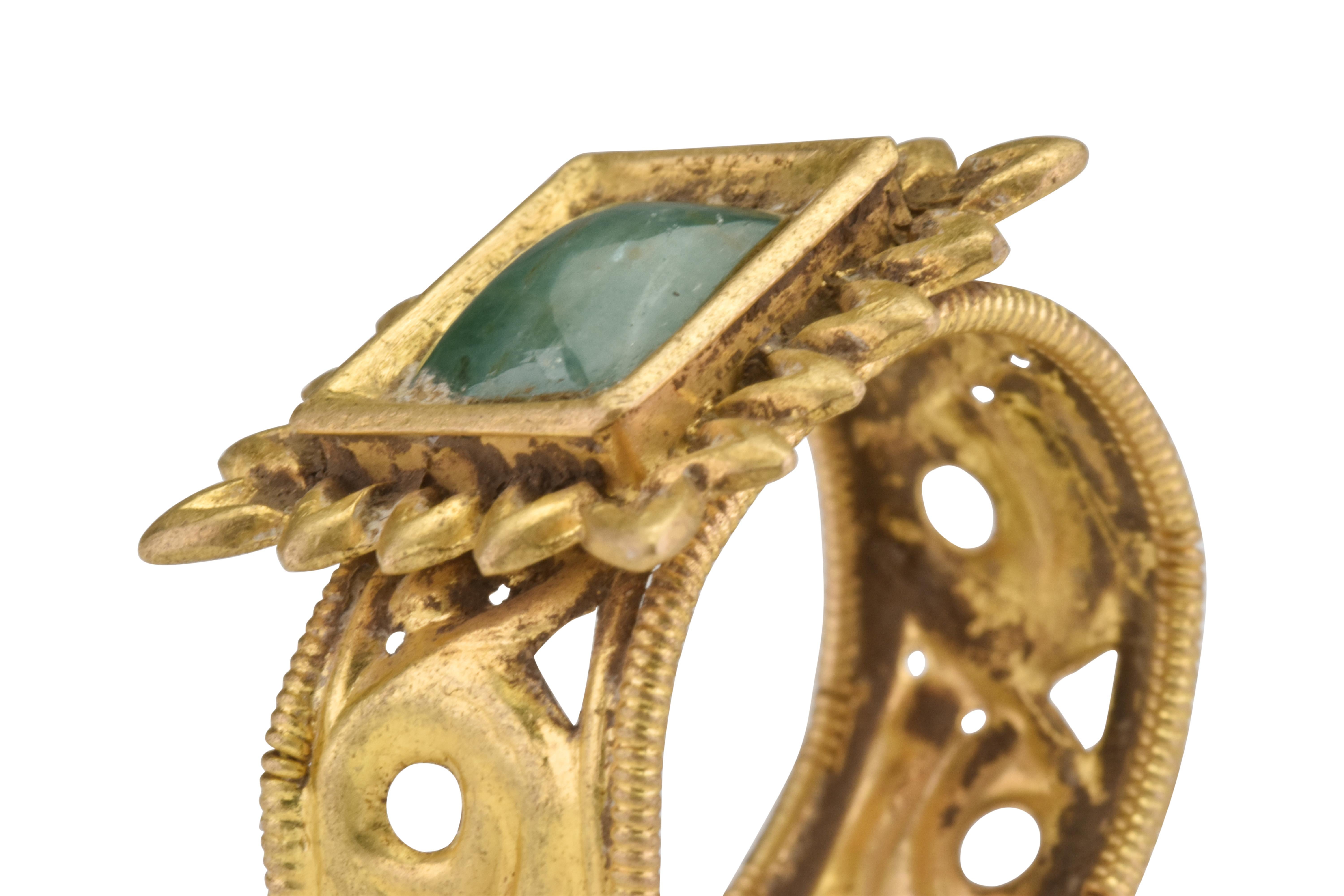 Ancient Byzantine Gold Ring with Emerald

Ca. 500 AD

A stunning gold finger ring comprised of a wide, flat-section band with beaded borders flanking an openwork design of scrolled decoration. The applied bezel consists of a rectangular plaque with