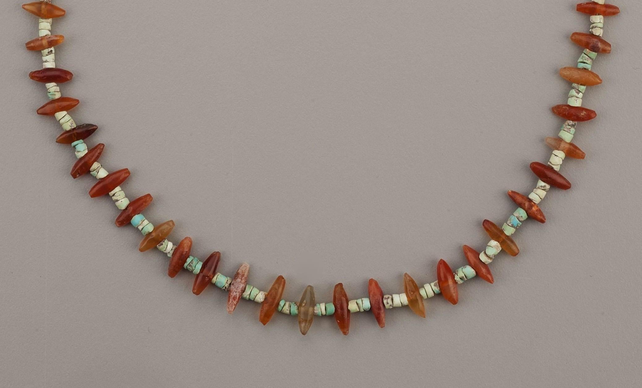 A necklace of fifty-two carnelian “spars” alternating with groups of three turquoise disc beads. The carnelian beads graduate slightly in size from the front of the necklace to the back. The height of the “spars” at the center is 1.2 cm and the