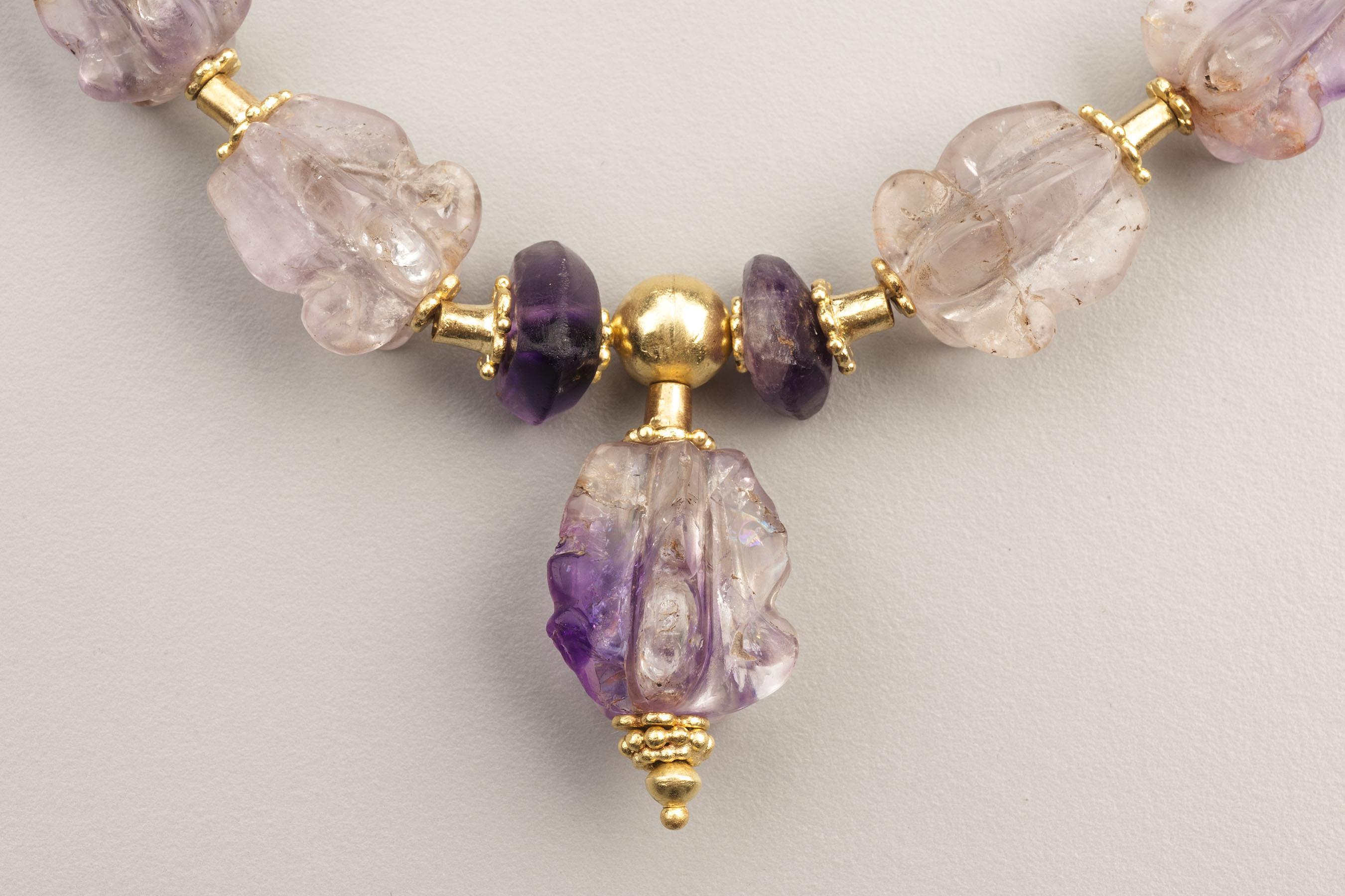 Twenty-three amethyst beads carved in the form of Crown flowers with five ridged lobes that flare on one end. There are four beveled triangular amethyst beads, two at the back of the necklace and two in the front on either side of the pendant bead. 