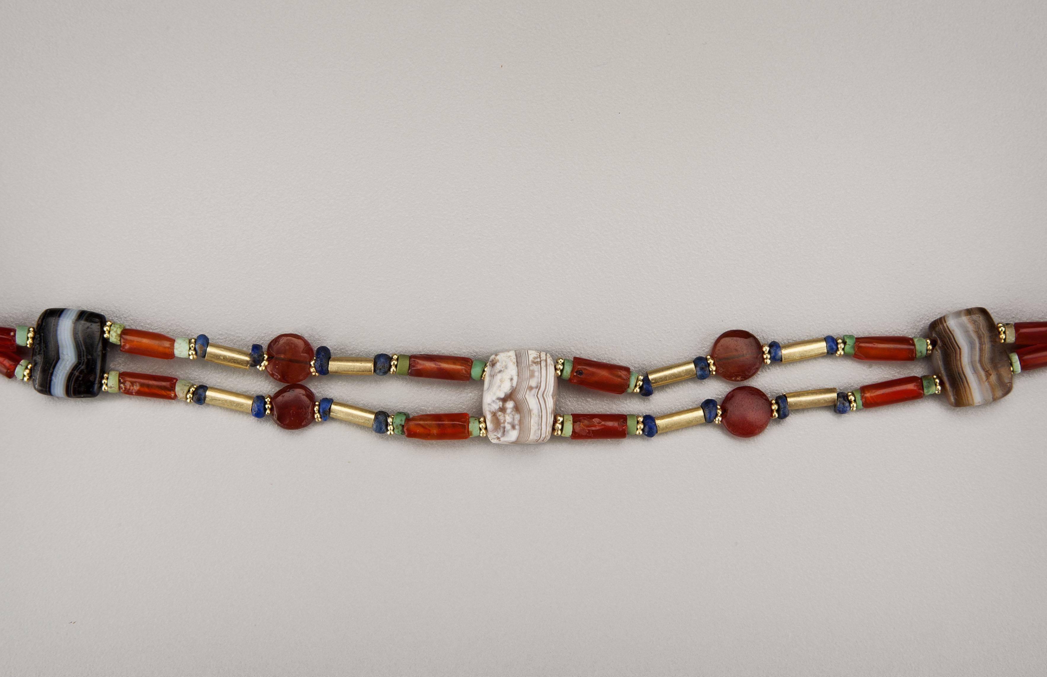 A choker style necklace of two connected strands of twenty cylindrical carnelian tube beads faced with turquoise disc beads, eighteen gold tube beads faced with lapis lazuli beads, alternating with eight tabular carnelian beads and five square flat