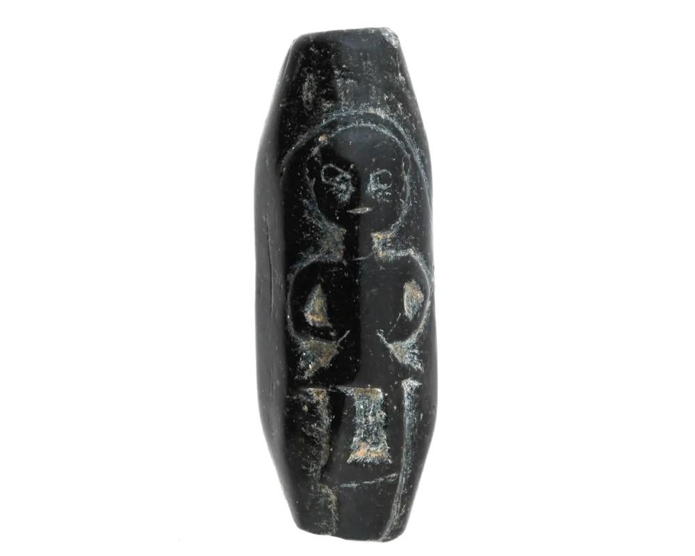 An ancient cylinder seal carved from black stone, bearing the image of mysterious figures. Crafted with intricate detail and precision, this seal captivates with its ancient charm and rich history. The figures depicted on the seal invites intrigue,