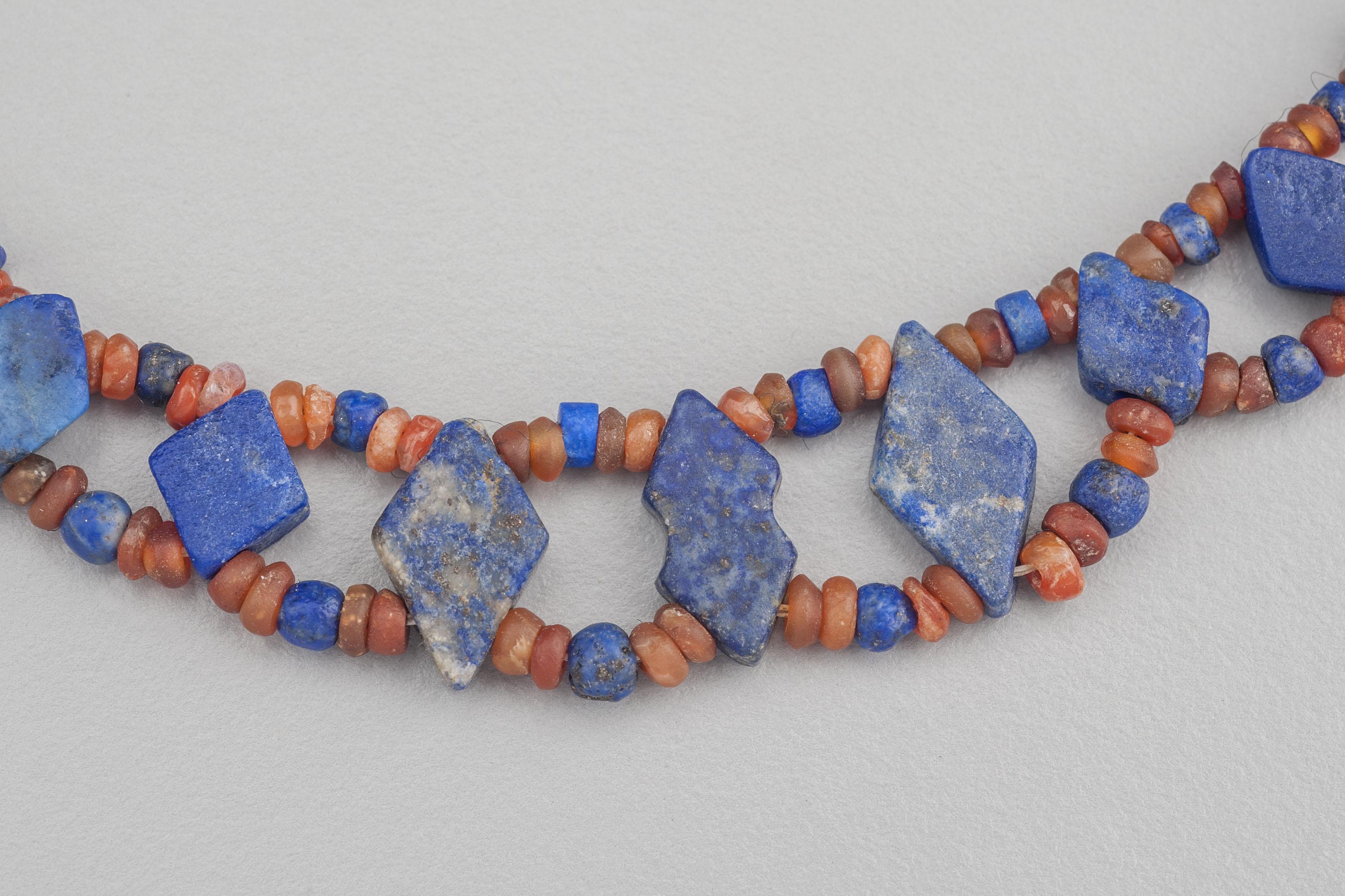 Thirty-three diamond shaped double-drilled lapis lazuli beads each of which is separated by two groups of four small carnelian beads with a lapis lazuli bead in the center. The diamond shaped lapis beads graduate slightly in size towards the back of