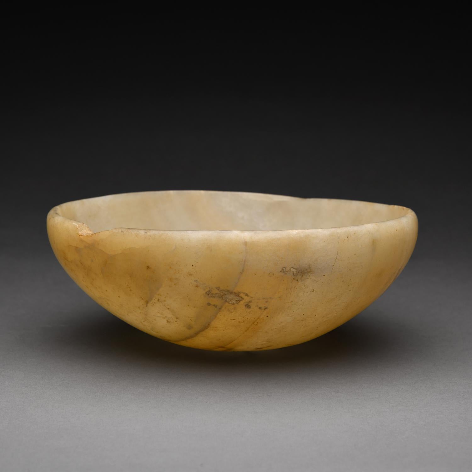 This elegant alabaster circular bowl is carved evenly throughout with thin walls displaying a beautiful translucence when exposed to direct light.  It features high curving sides, a gently inward sloping rim, and a rounded base. Rich caramel bands
