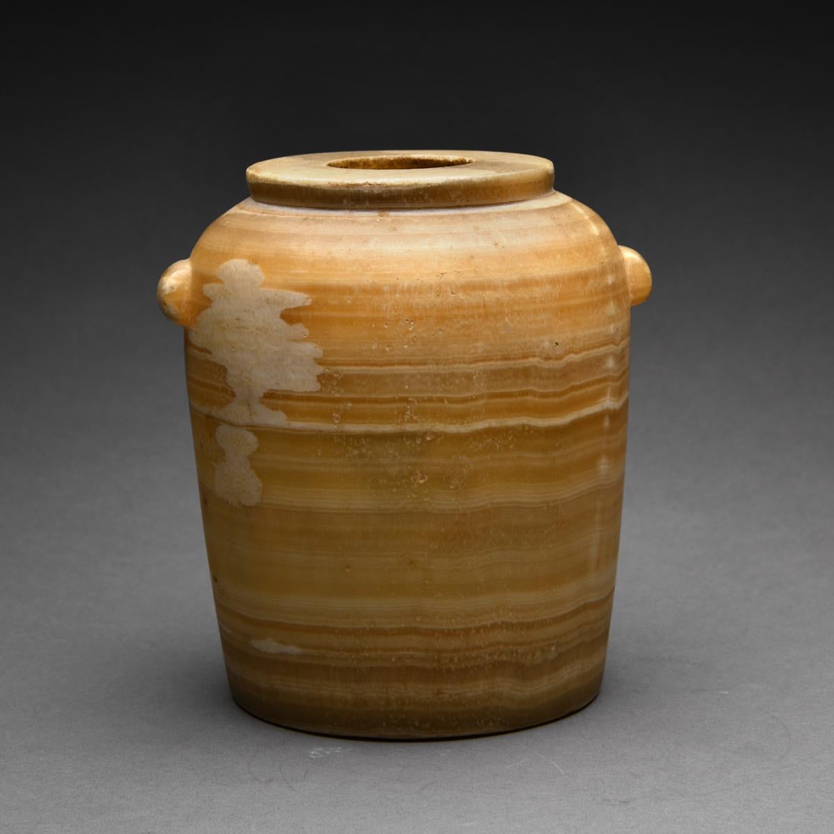 A large, and very fine barrel-shaped jar of alabster with well defined bands of creme and caramel highlights. Twin vestigial lug handles are located on each side below a wide disc rim.

Notes

Egyptian alabaster is a form of limestone or calcium
