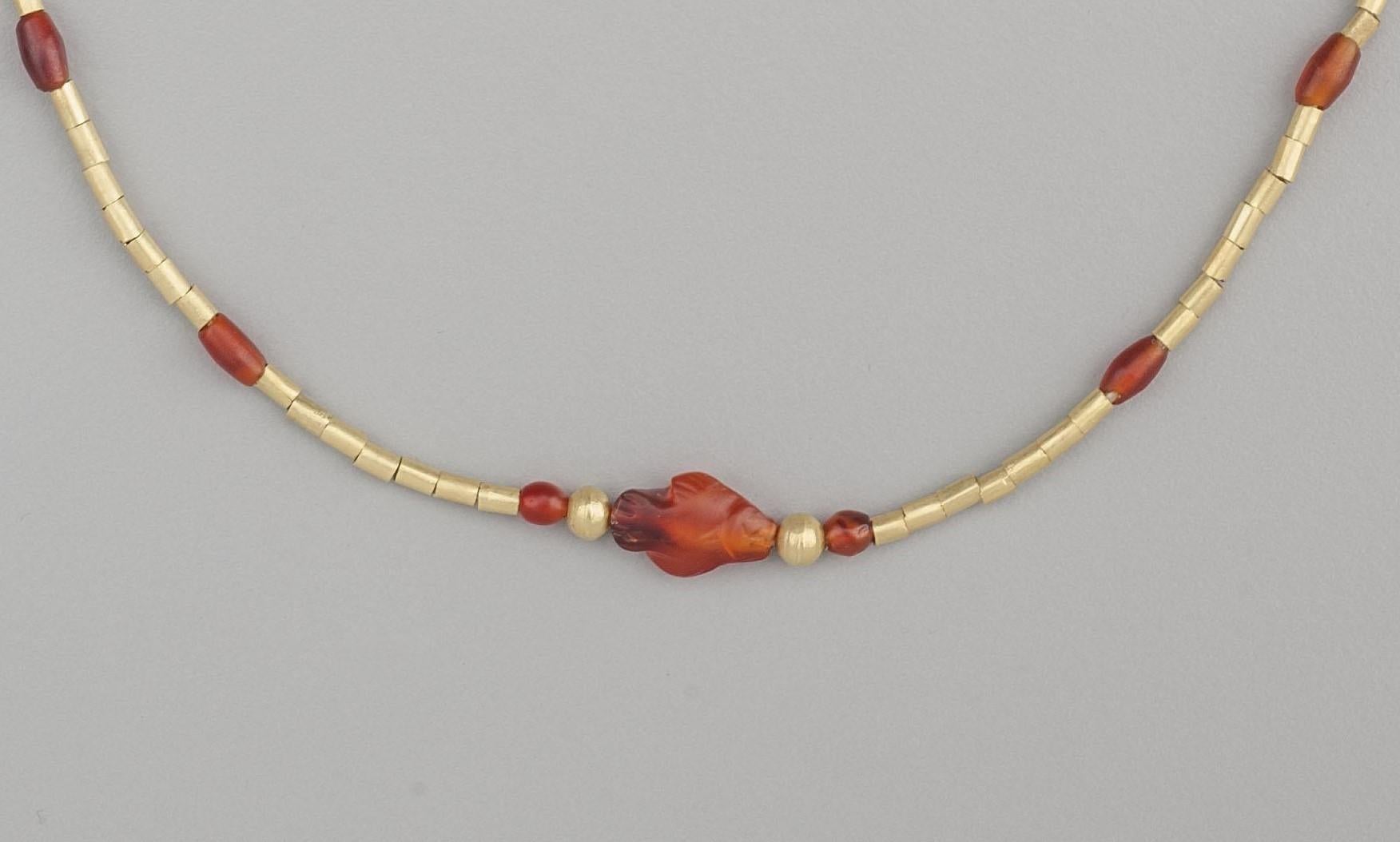 Ninety-six 20k gold tube beads, fourteen carnelian barrel beads, and a carved carnelian fish amulet faced on each side with a pair of spherical 20k gold beads. Gold beading tips and a hook and eye clasp complete the strand. The fish bead is 1.45 cm