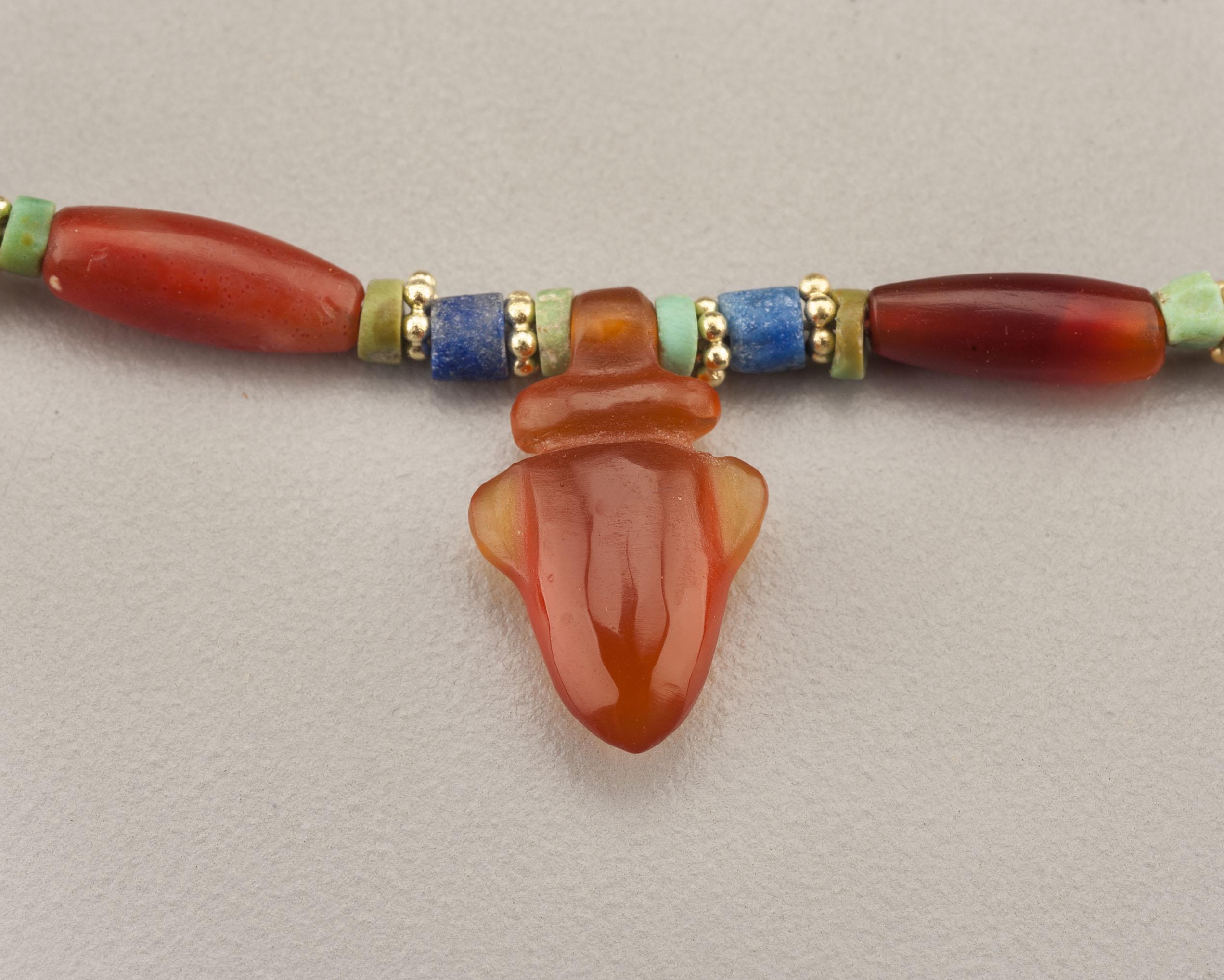 Carnelian, turquoise and lapis lazuli beads with fourteen poppy seed pod pendants and a carnelian heart amulet pendant. The necklace is accented with seventy-two granulated 20k gold ring beads. There are twenty-two carnelian barrel beads alternating