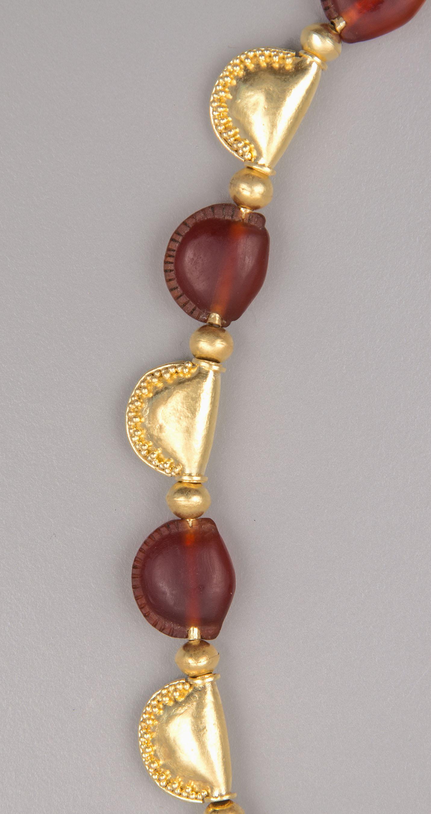 Eleven ancient carnelian beads and ten gold beads, all shaped to resemble cowrie shells. There are twenty-two spherical gold beads alternating between the shell beads. There are stirrup beading tips at each end which provide attachment loops for the