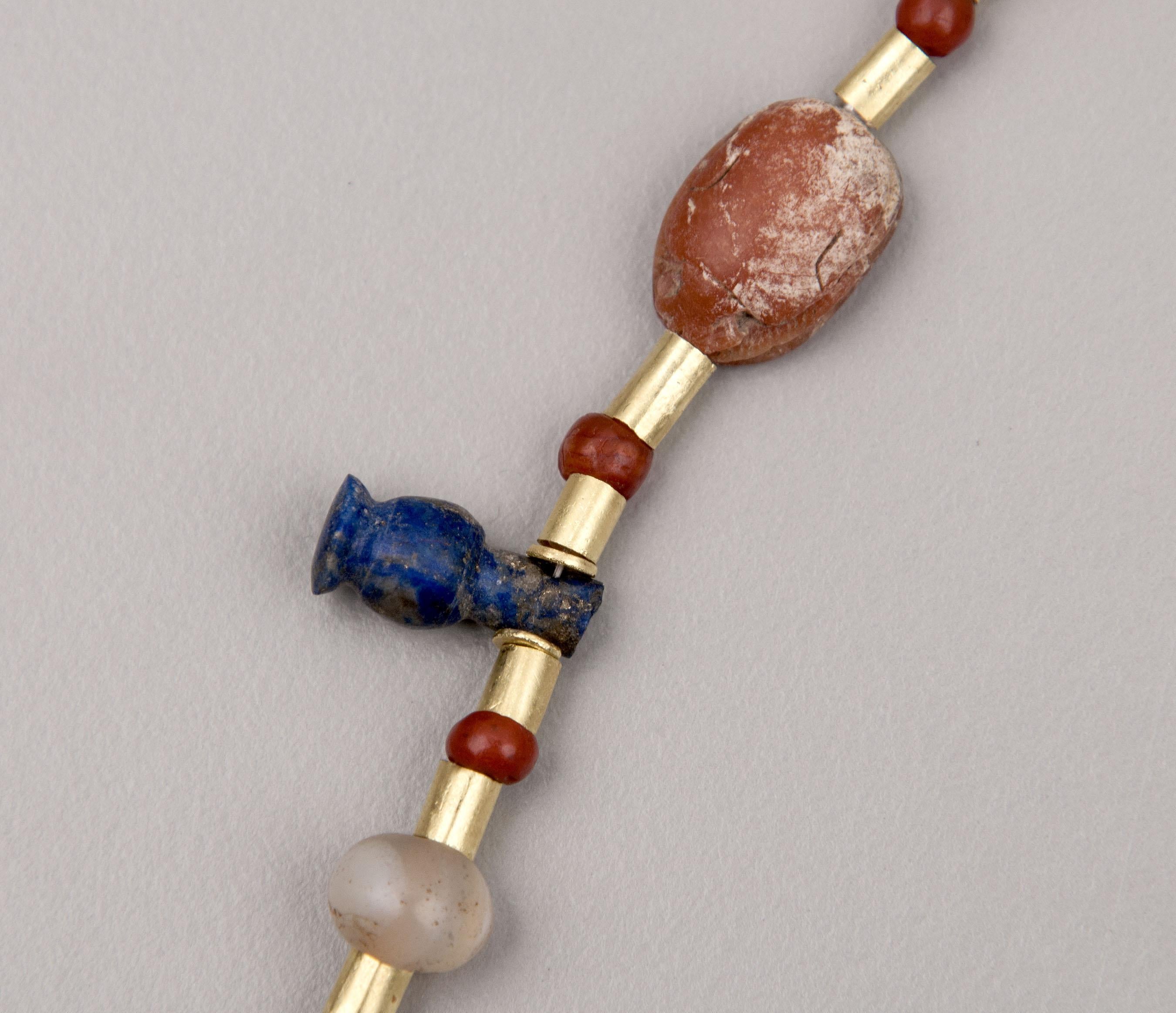 Thirty-six small round, carnelian beads and thirty-two larger beads and amulets of various materials such as carnelian, agate, amethyst, lapis lazuli, diorite, feldspar and faience. Each of these stone beads are alternating with 20k gold tube beads,