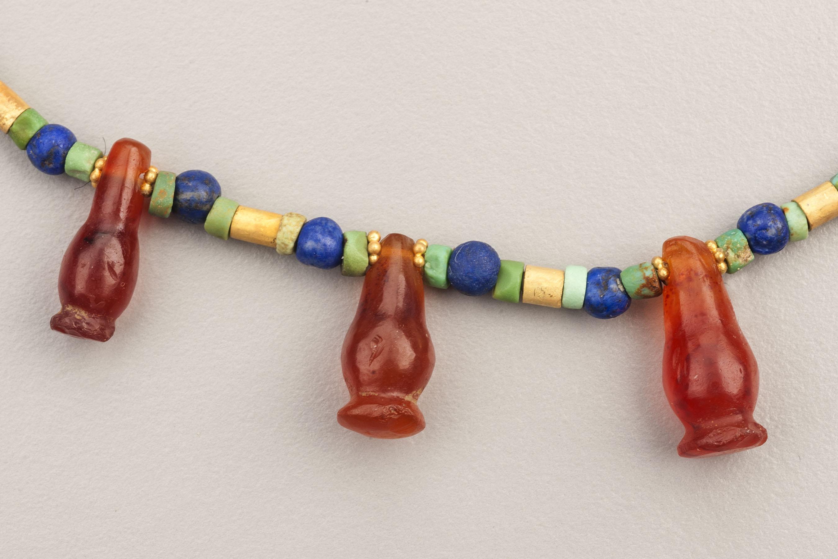 Gold, lapis lazuli, turquoise and carnelian beads, including fourteen carnelian poppy seed pod pendant beads. The largest of these is 1.7 cm in height and 7 mm in width. The smallest carnelian poppy is 1.25 cm in height and 6.3 mm in width. The