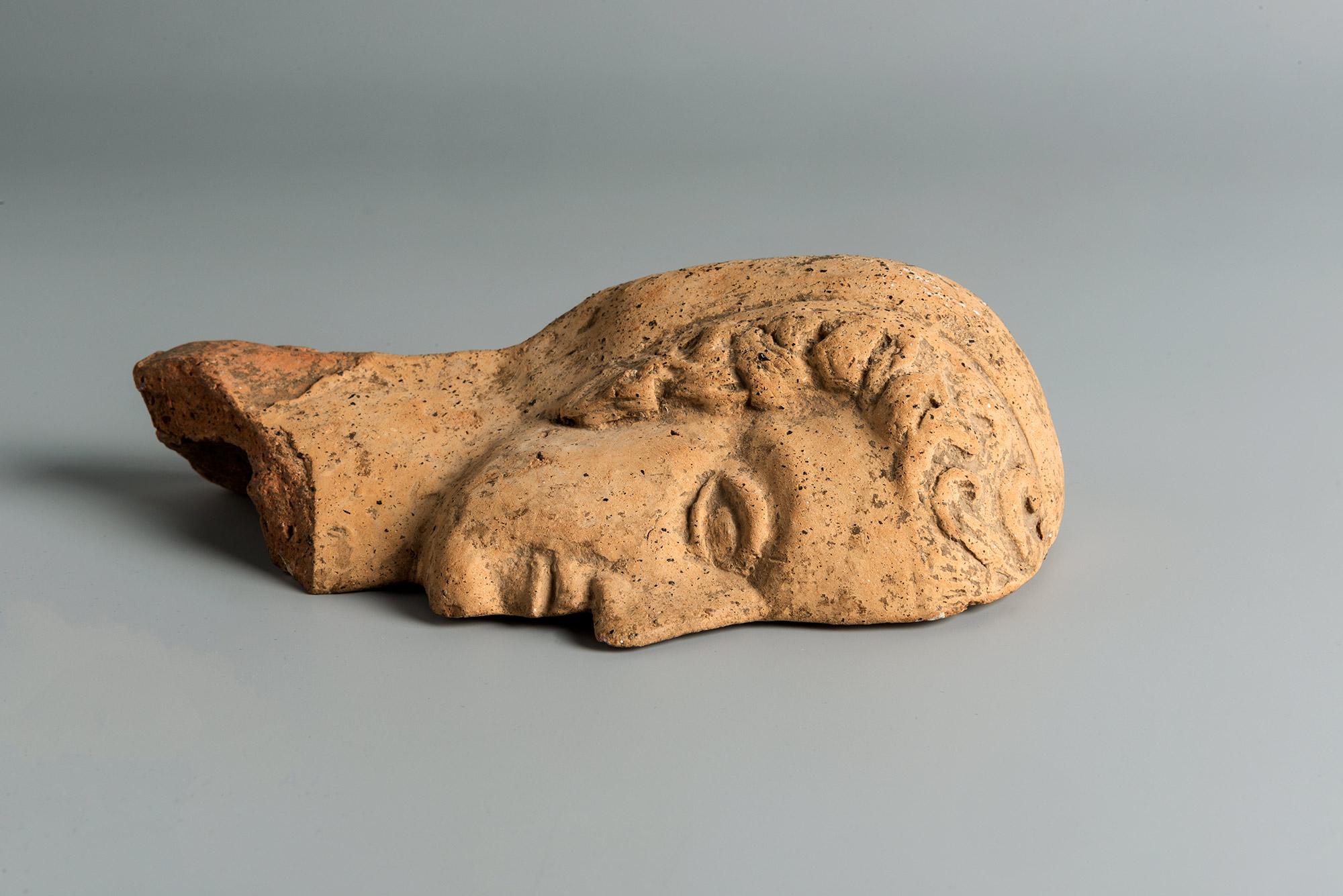 The Votive shows a female head in profile. The face with the almond shape eye is finely detailed with her curled hair coming from under a veil. On the reverse the Votive is hollow where a hook is attached for hanging. The object is intact as