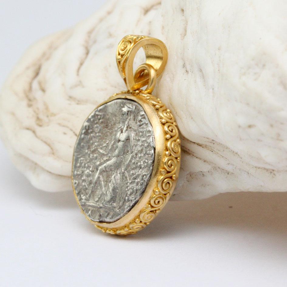 Una moneta d'argento autentica e ben coniata, risalente all'antico regno greco seleucide del 152-145 a.C., raffigura il dio Apollo seduto, con in mano una freccia e un arco circondati da scritte greche orientate verticalmente.  Il rovescio è