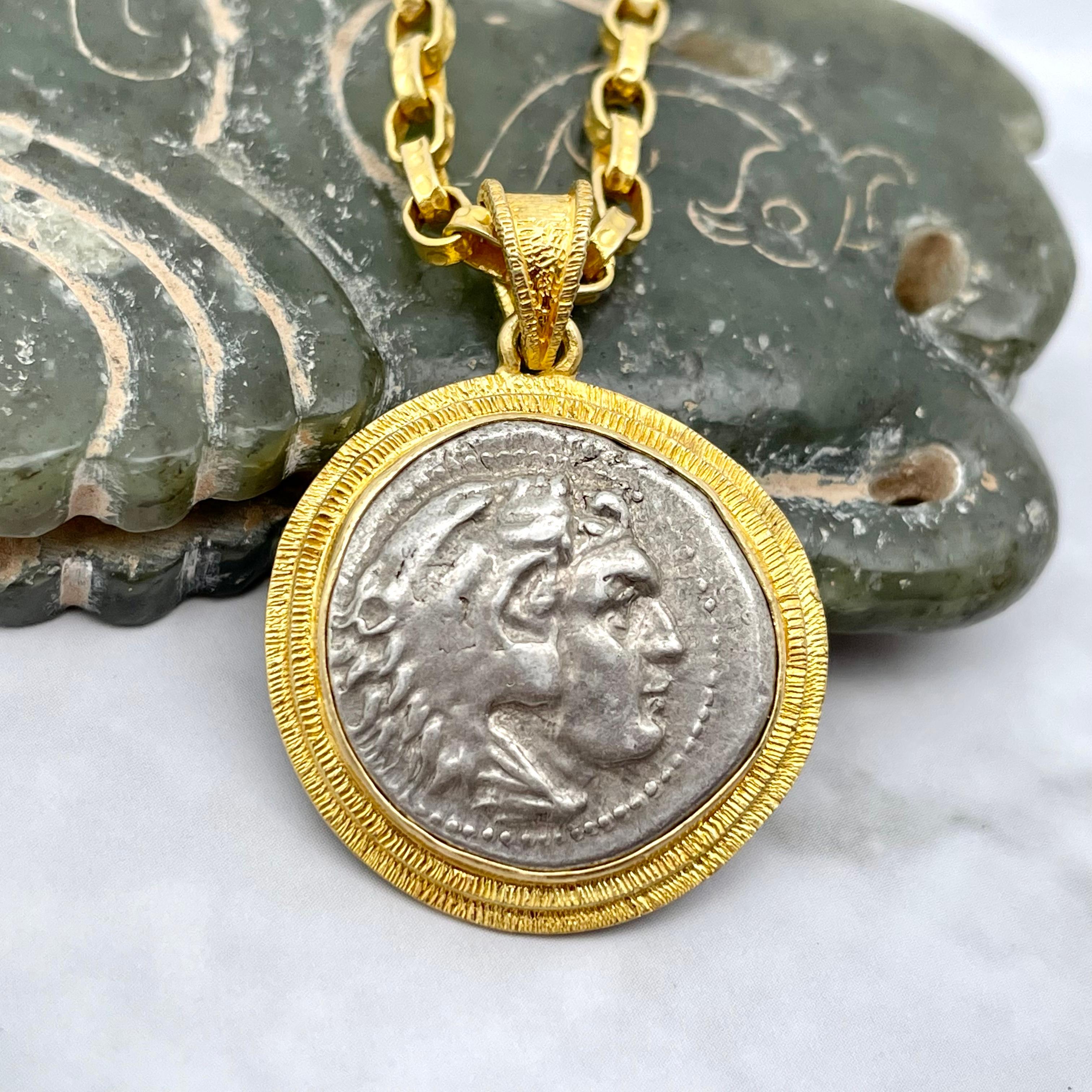 Une authentique pièce de monnaie de l'Antiquité grecque, le drachme, représentant le buste d'Hercule, est sertie dans une double ligne de texture dans ce design simple, mais visuellement attrayant, de Steven Battelle. Hercule est vêtu de la cape en