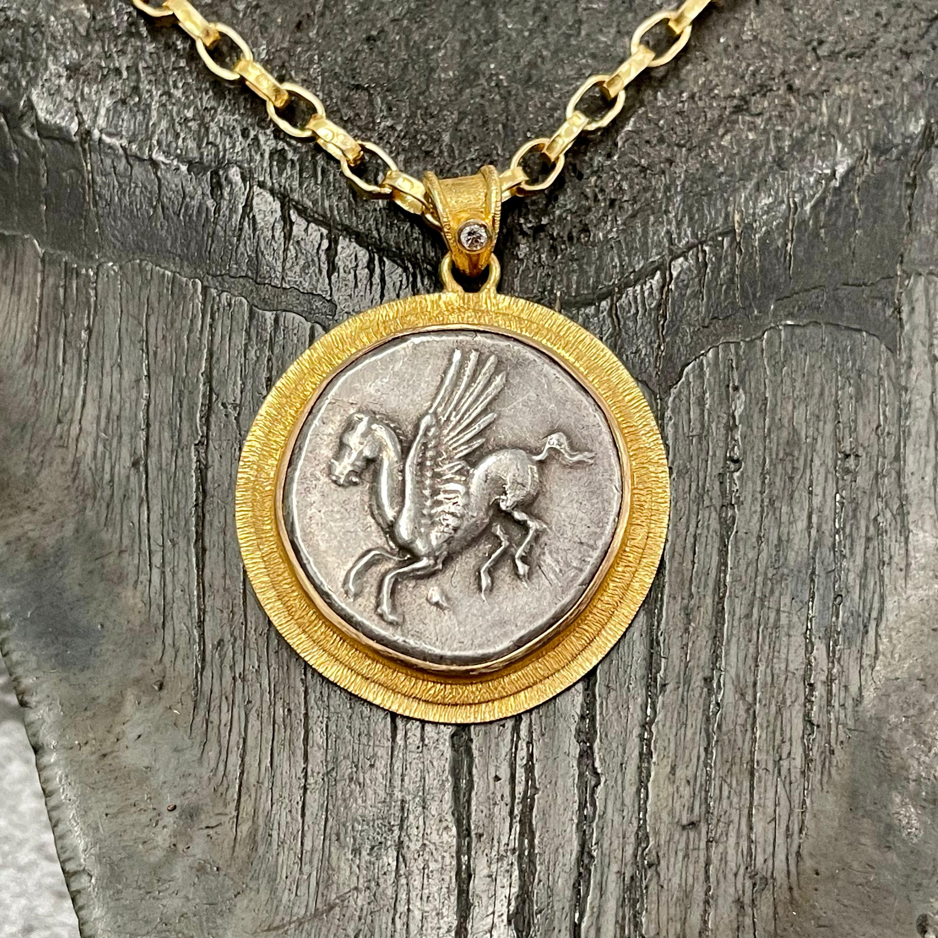 An authentic Corinthian Stater coin from 375-300 BC is showcased in a Steven Battelle designed double line texture bezel with a 1.8 mm diamond accent on the bail.  This is the classical image of Pegasus known throughout the ancient world.  The