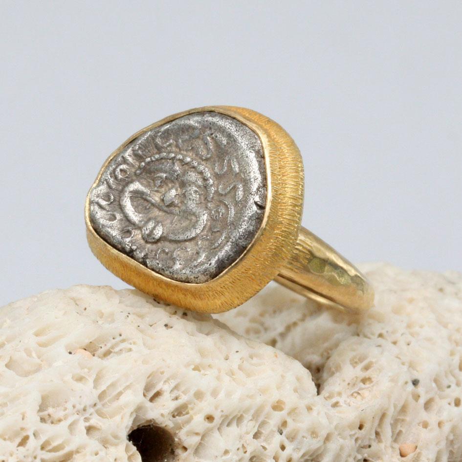 An authentic ancient Greek Coin from 450-400 BC featuring the face of Medusa with her protruding tongue and crown of snakes is set surrounded by a stepped and line textured bezel in this Steven Battelle design. This coin depicts Medusa – the only